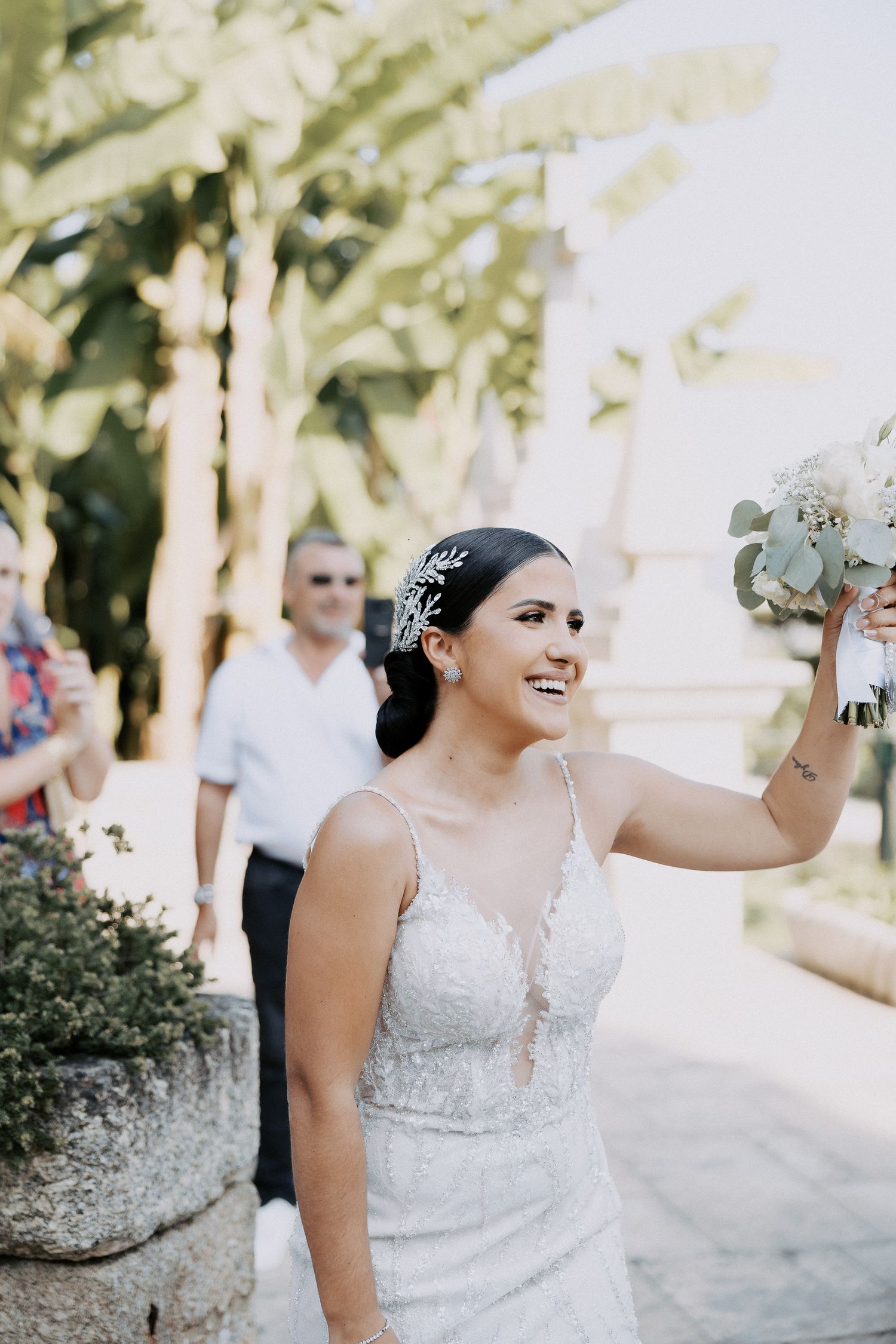 A bride in a beaded white wedding dress laughs joyfully during an outdoor celebration.