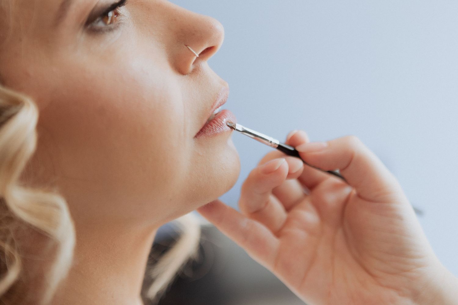 Maquiadora profissional aplica brilho labial com um pincel pequeno durante ua preparação da noiva.