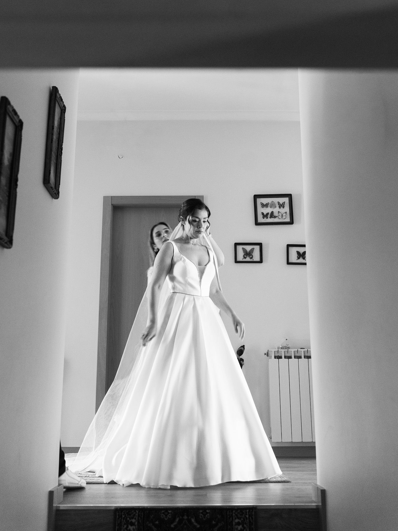 Black and white photo of a bride in a elegant ball gown wedding dress standing in a room during bridal preparations.