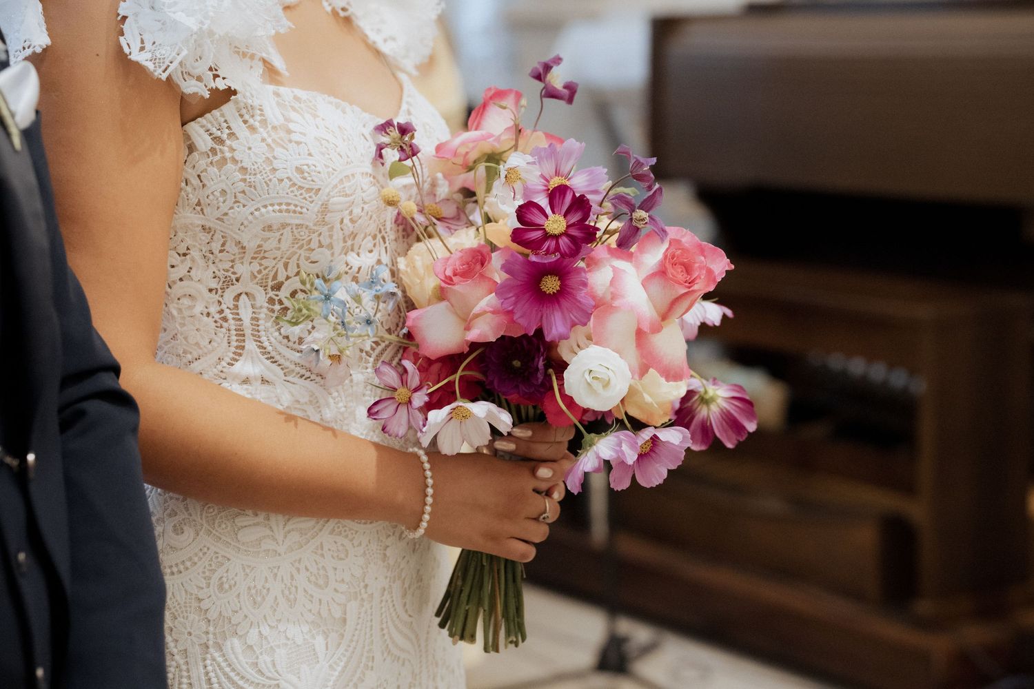 Buquê de noiva com orquídeas rosa e hortênsias brancas sobre um vestido de noiva de renda. Casamento na Quinta do Cruzeiro.