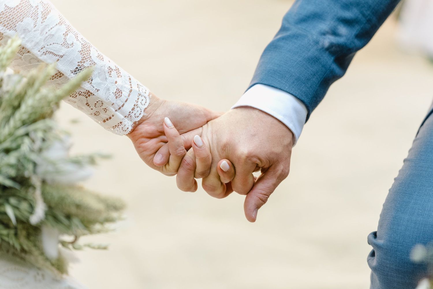 Close-up of hands exchanging wedding rings during an outdoor ceremony with sunlight filtering through.