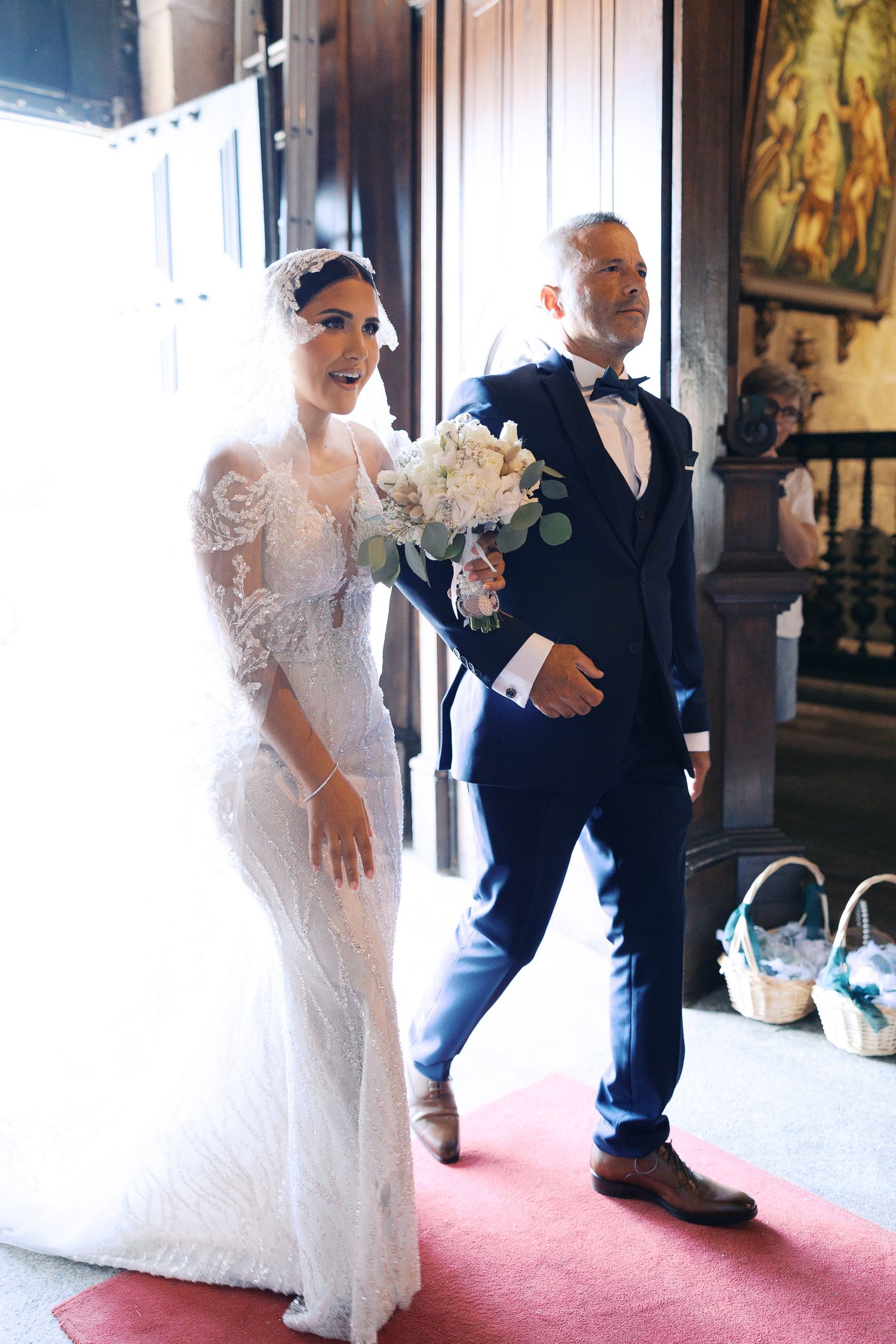 Wedding couple shares a playful moment in an elegant venue with ornate decor and red carpet.