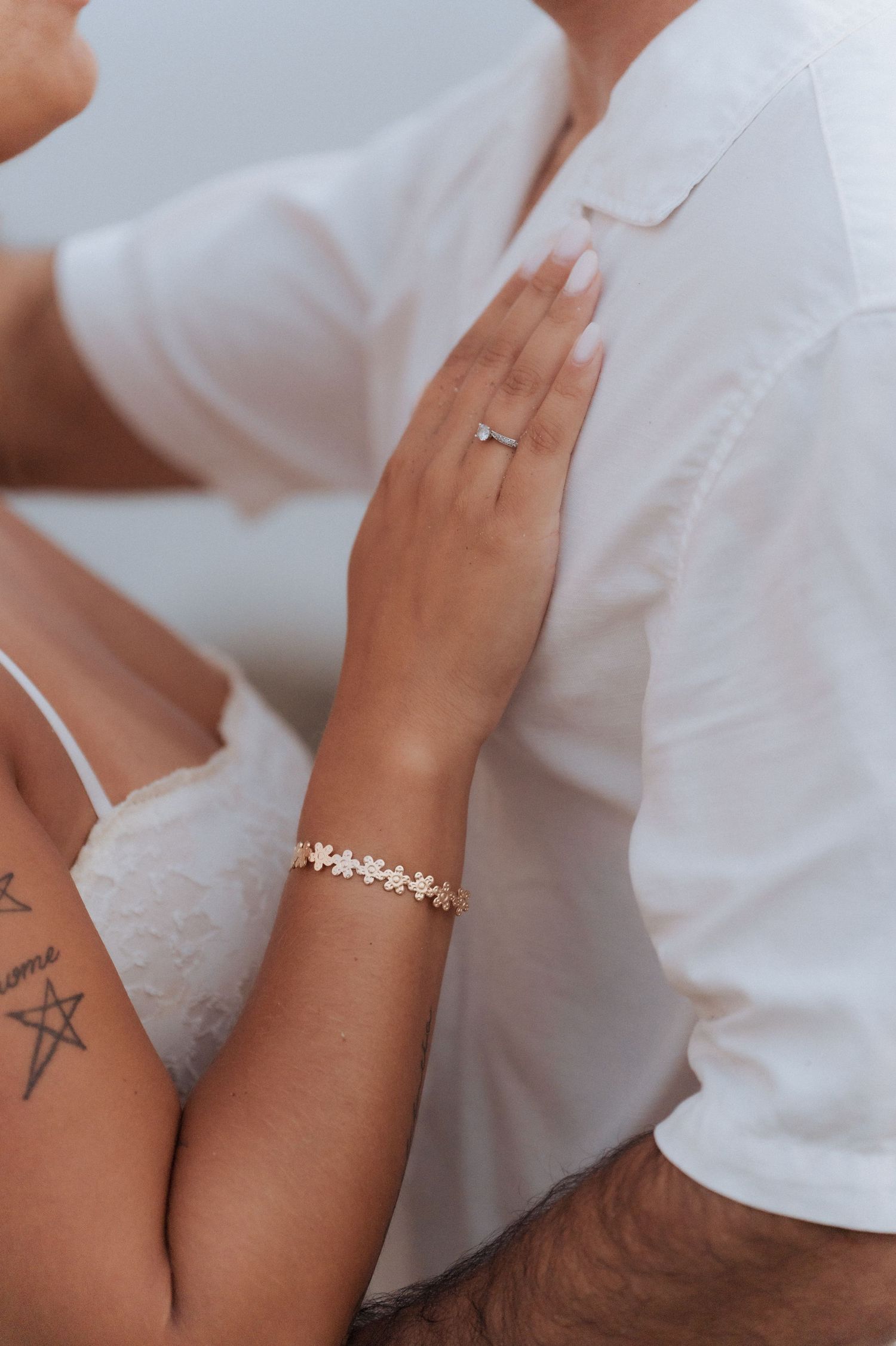 Detalhe em close-up de mãos com joias delicadas e pequenas tatuagens sobre tecido branco. Sessão fotografica de namoro