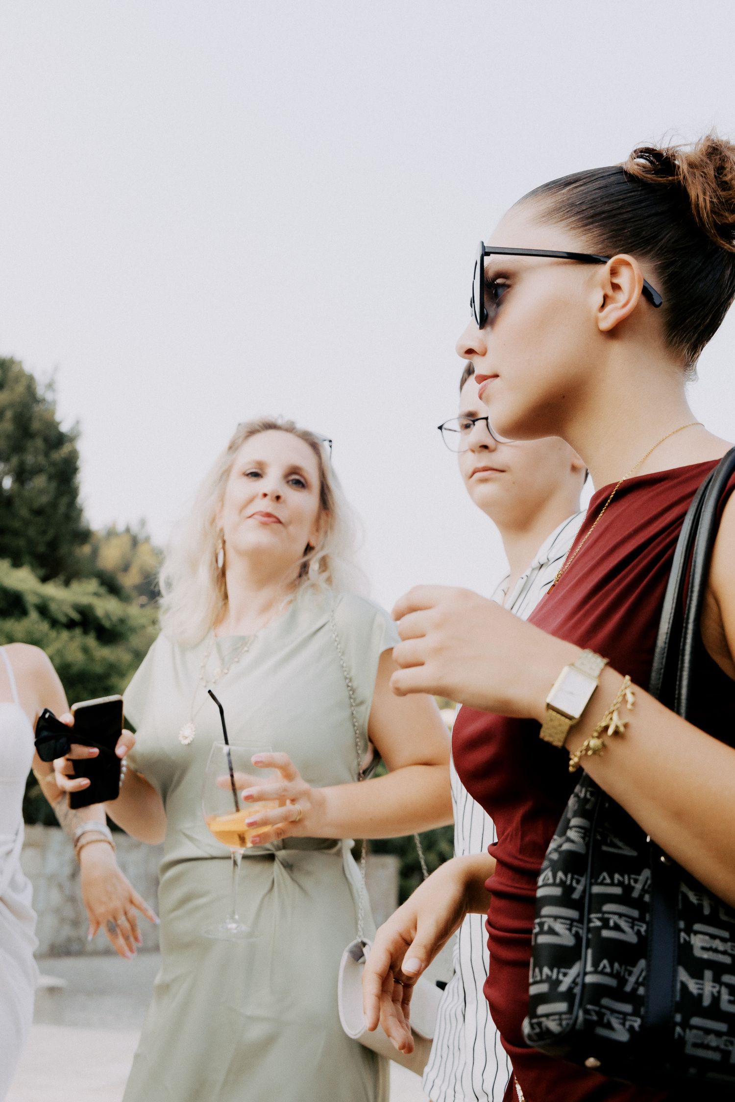 Two friends walking outdoors while holding drinks and phones on a sunny day.