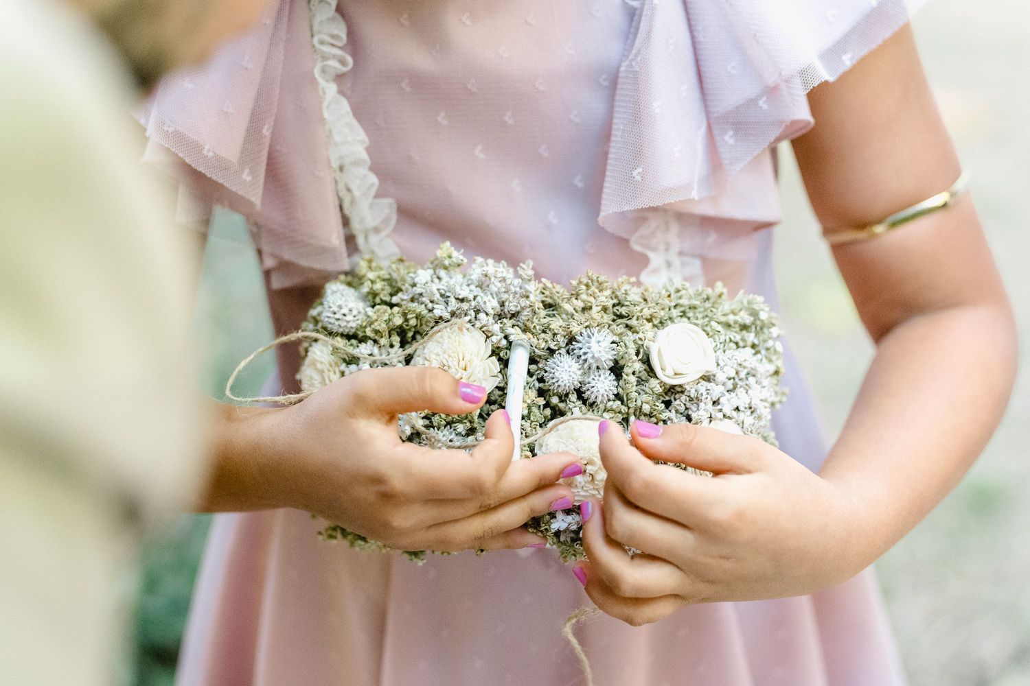 menina segura um pequeno ramo de flores brancas e verdes nas mãos, sobre um fundo claro. casamento numa quinta em ponte e lima