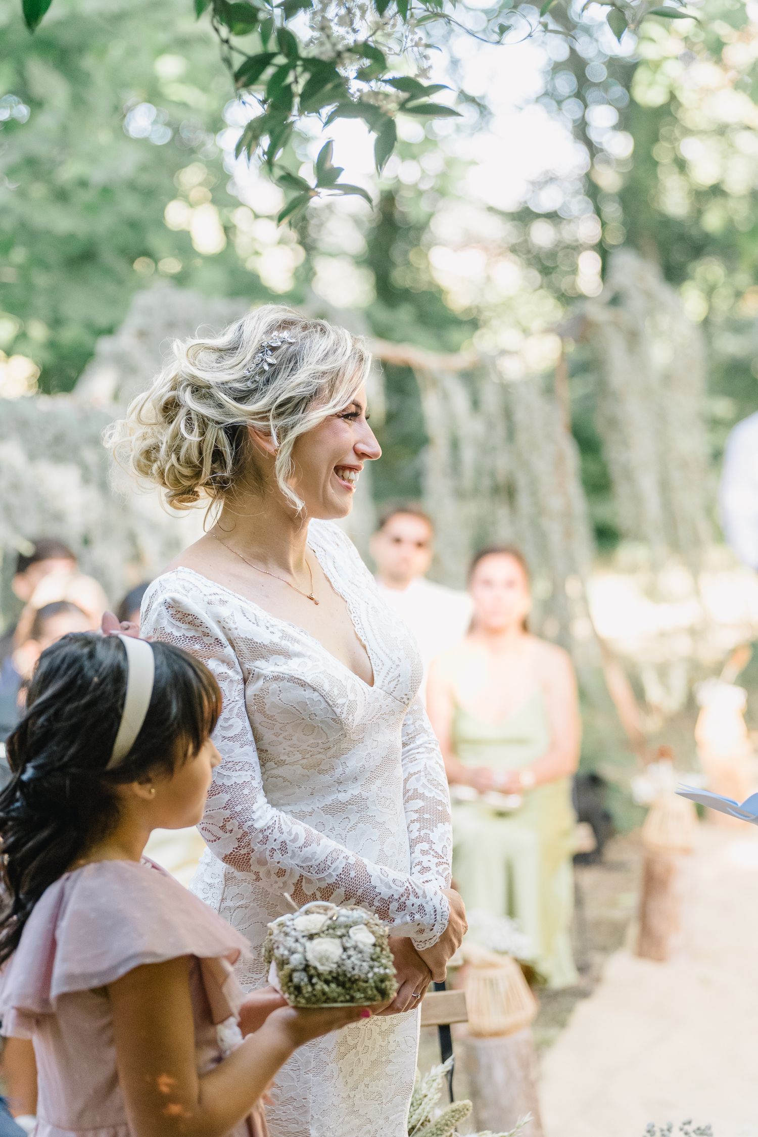 A joyful moment captured between a bride in a lace dress and guests during an outdoor forest wedding celebration.