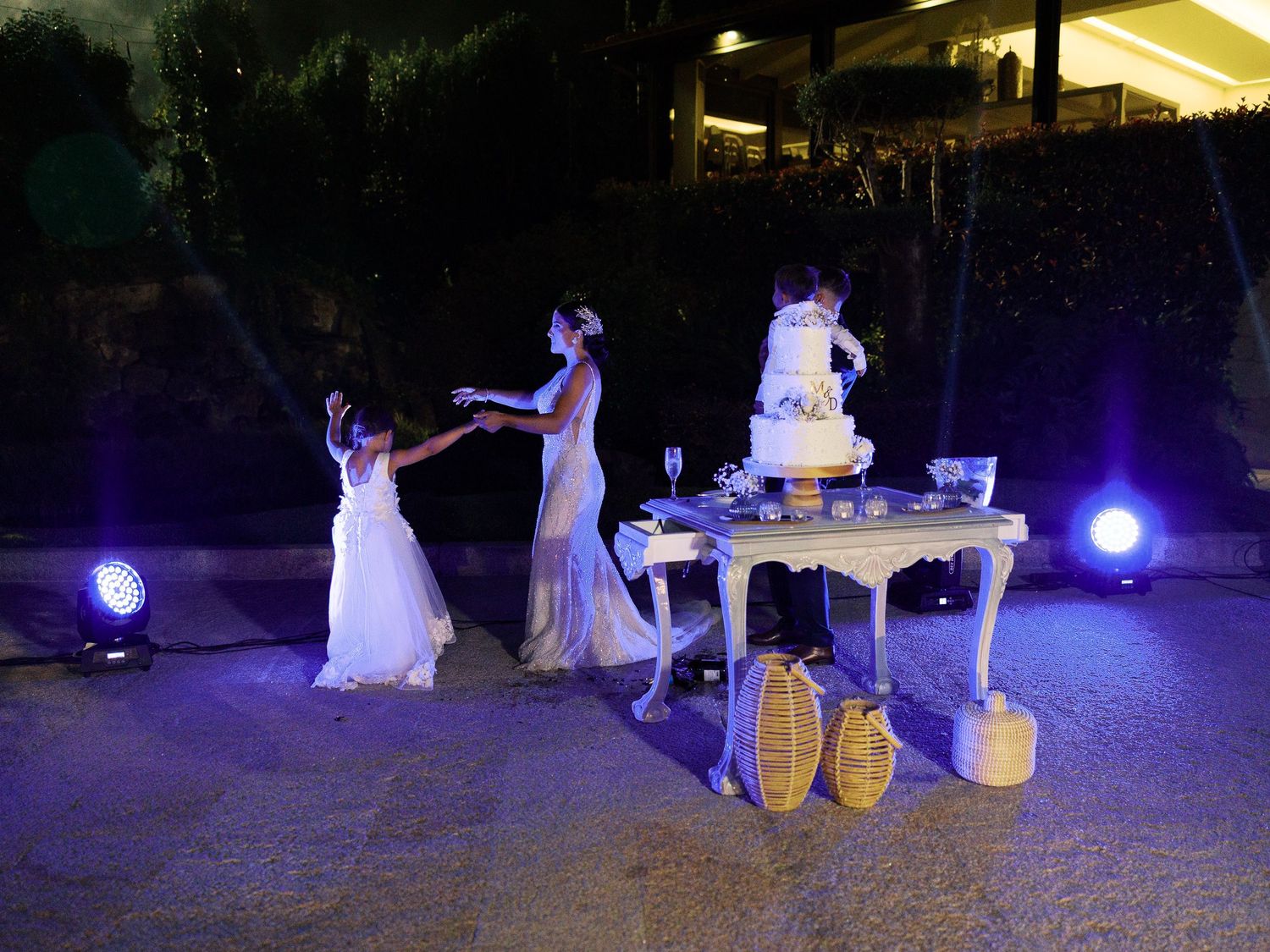 A nighttime wedding reception scene with people dancing near an illuminated cake table with purple lighting.