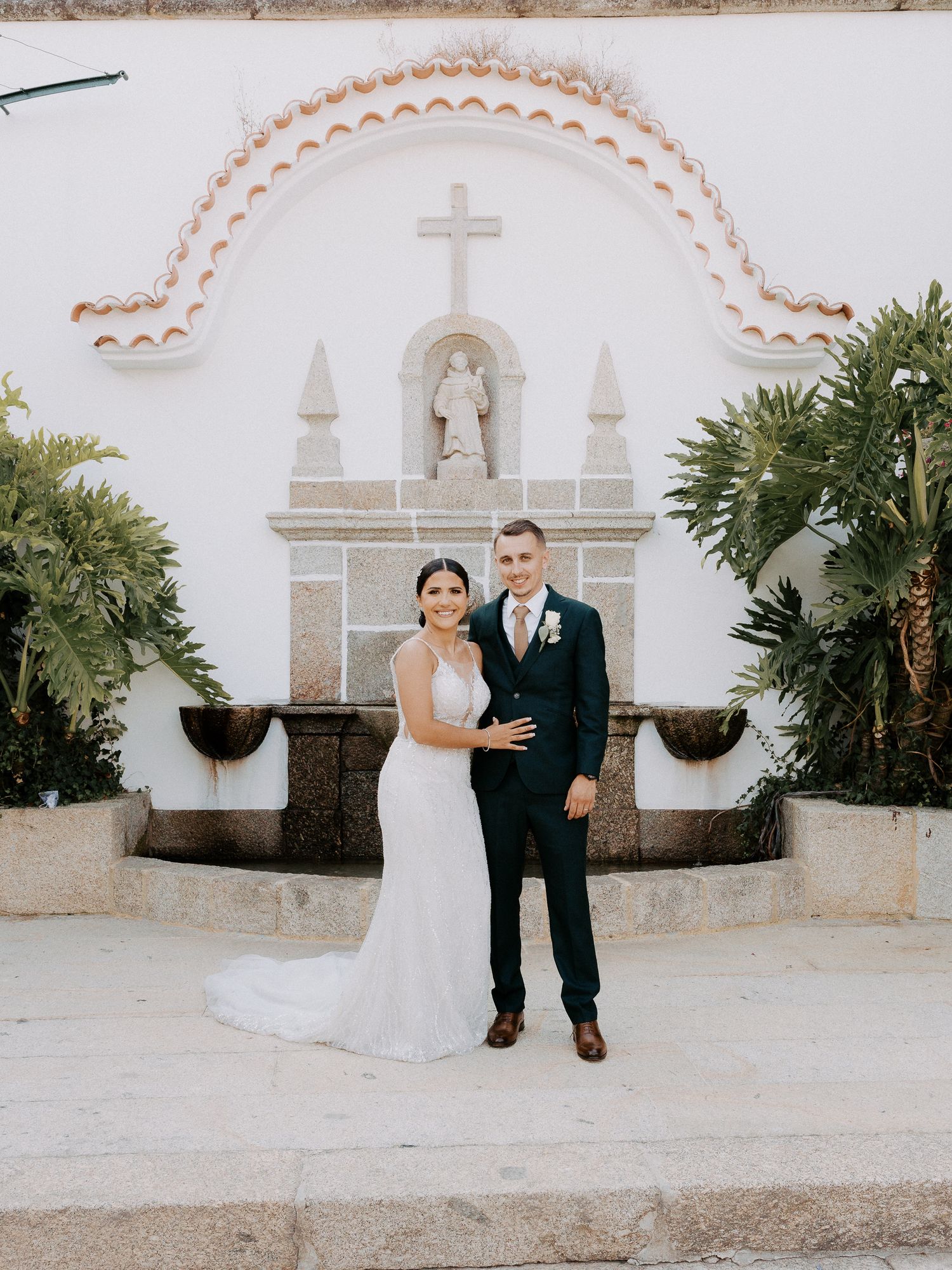 Newlywed couple shares romantic moments in front of a white Spanish colonial church with decorative arches and palm plants.