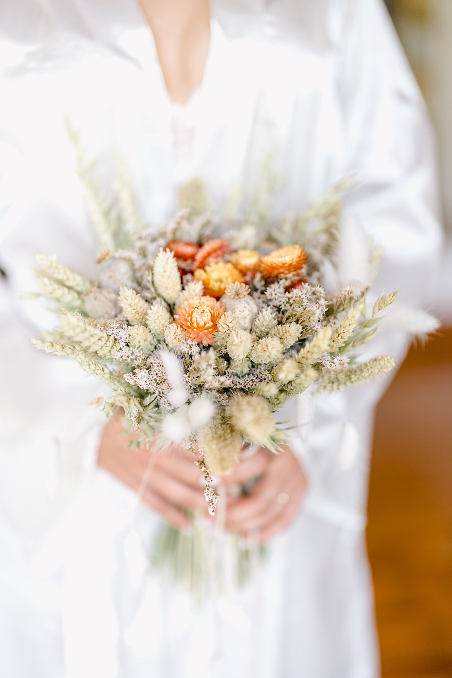 Close-up view of delicate dried flower wedding bouquet with white and peach blooms held against white fabric.