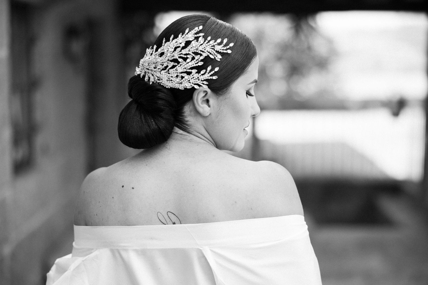 Black and white photo of bride in off-shoulder wedding dress with elegant updo hairstyle.