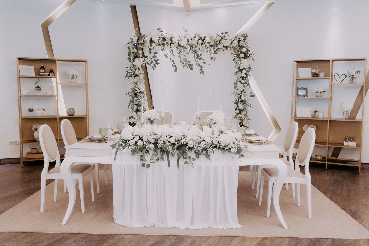 Modern white event space with draped fabric decor, floral arrangements, and wooden shelving displays.