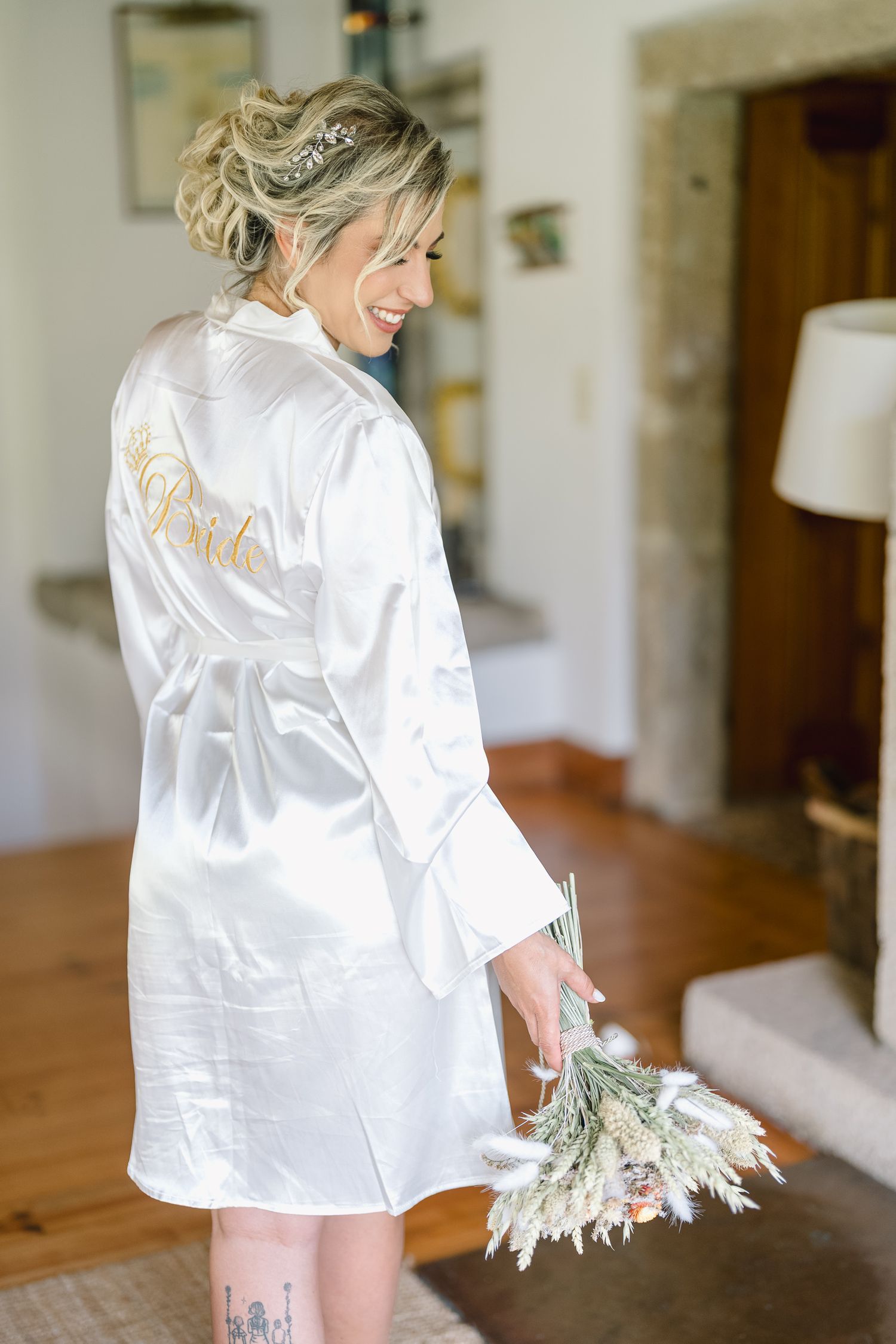 A person wearing a white silk robe stands by a wooden table in a bright, minimalist interior space.