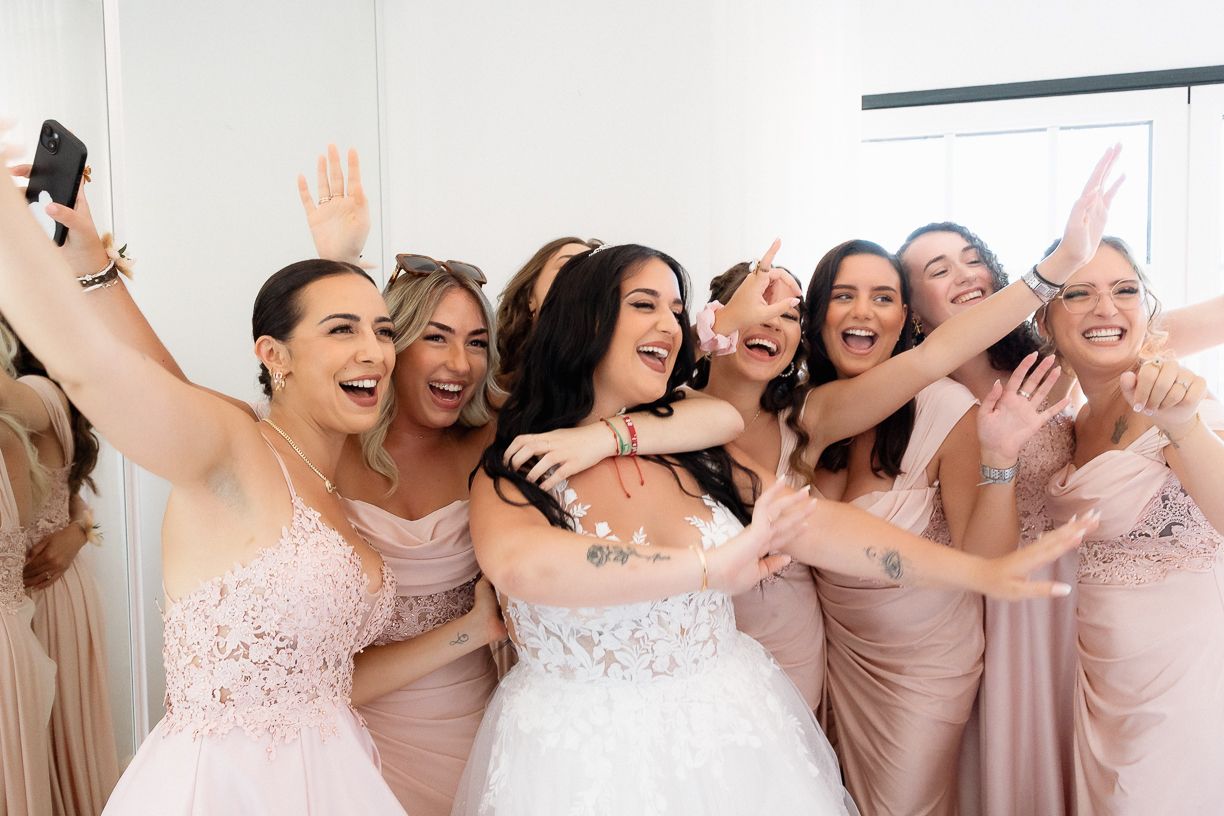 Um grupo de damas de honor vestidas de rosa riem juntas enquanto tiram uma selfie durante uma festa de casamento. Quinta de Santo André