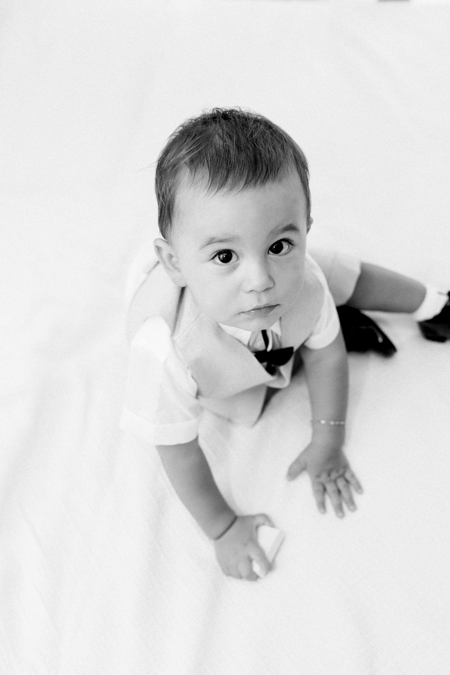 Black and white portrait of a baby in white clothing crawling on a light background.