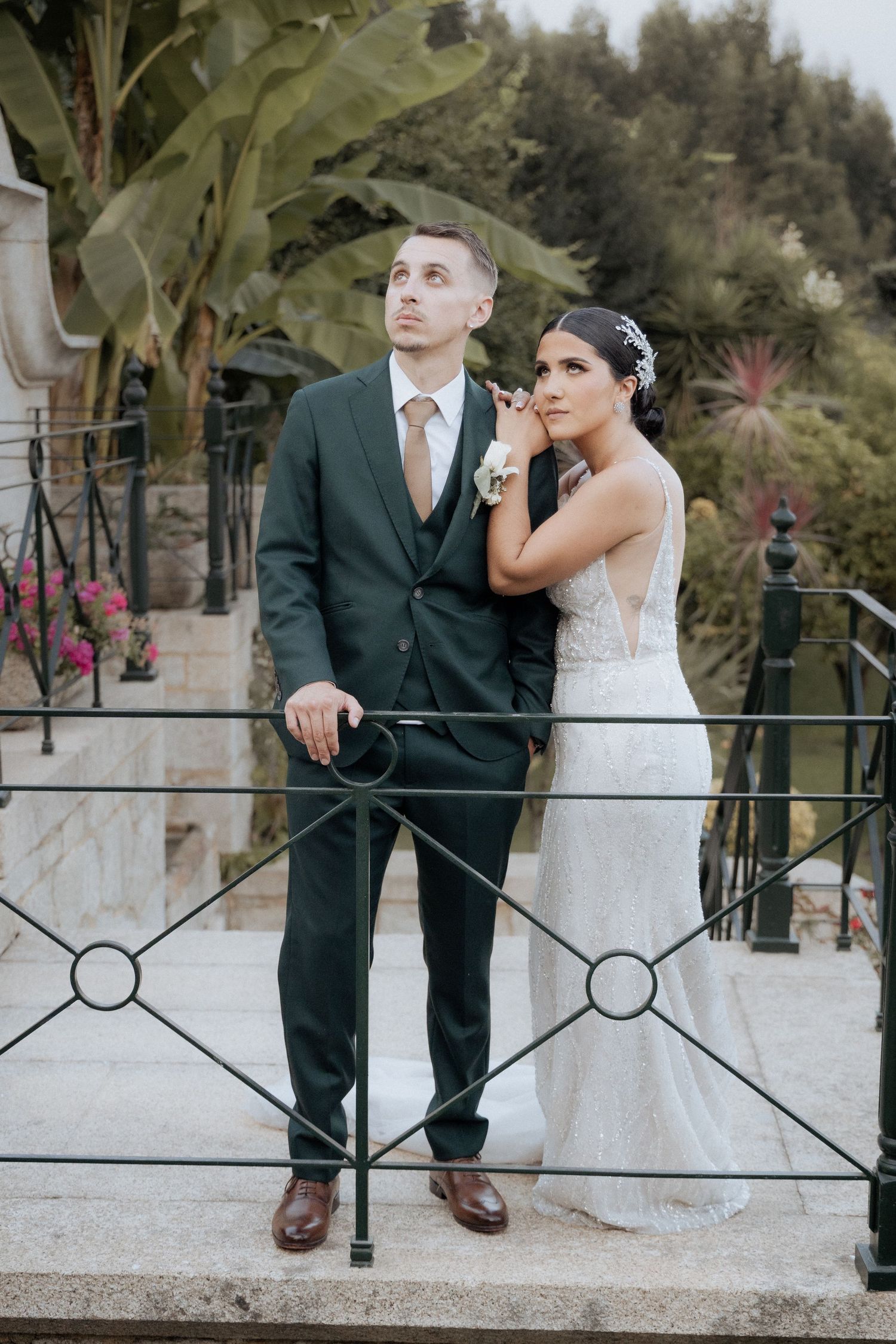 Casal de noivos posando junto a uma grade de ferro decorativa em um jardim na Quinta da oia Barcelos