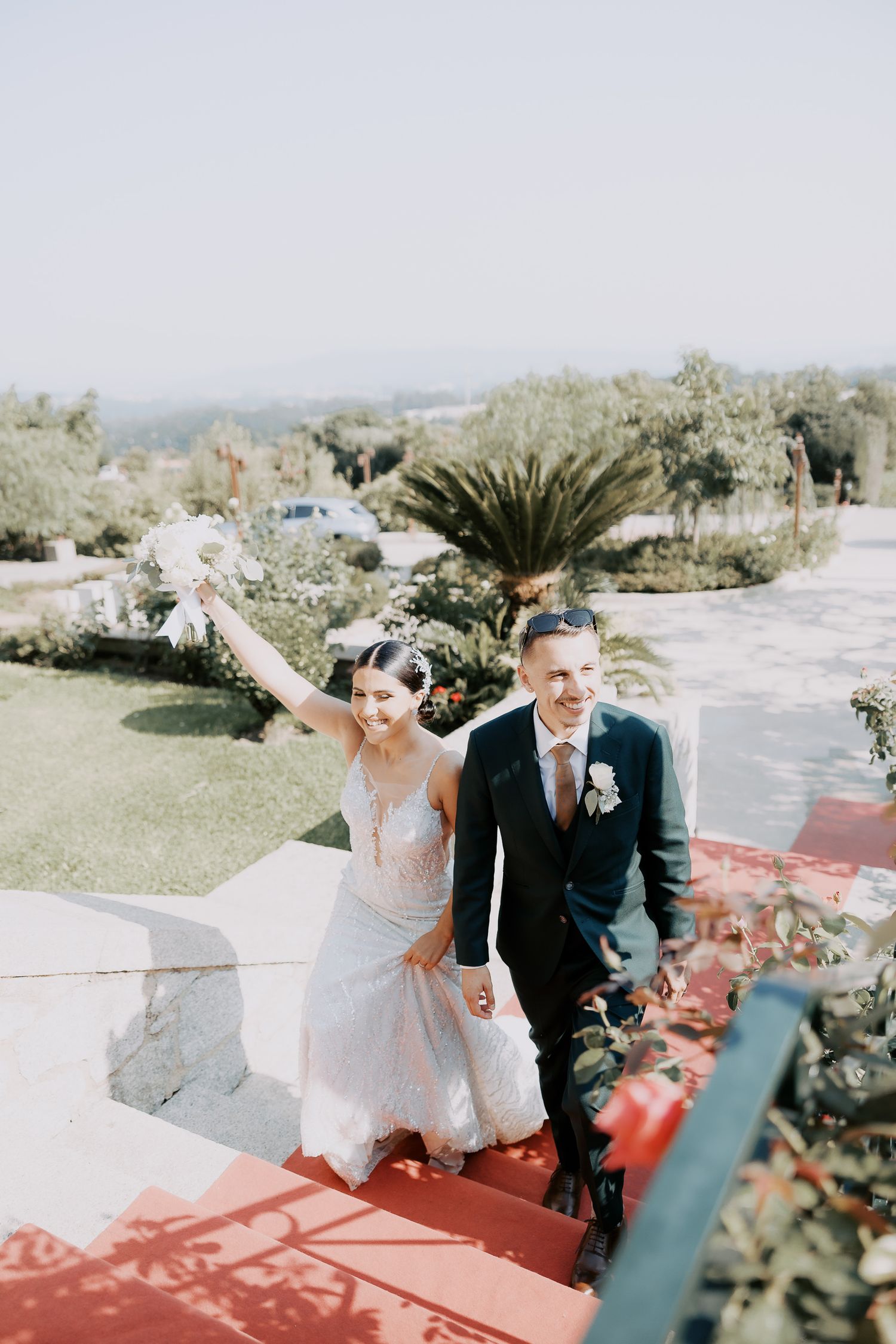 A couple celebrates joyfully on their wedding day with a scenic outdoor backdrop of palm trees and greenery.