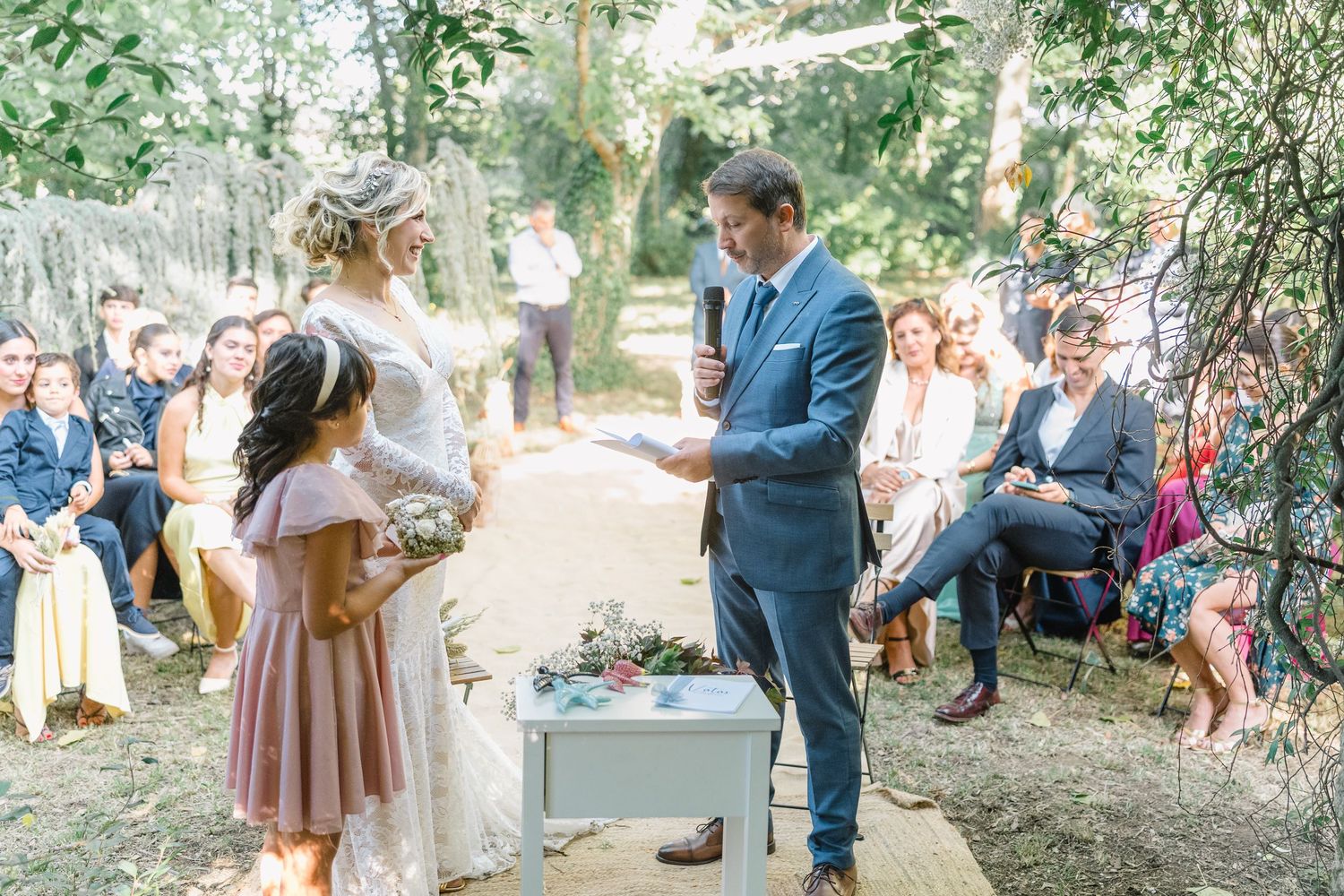 Wedding guests gather outdoors under trees for a casual summer celebration with drinks and conversation.