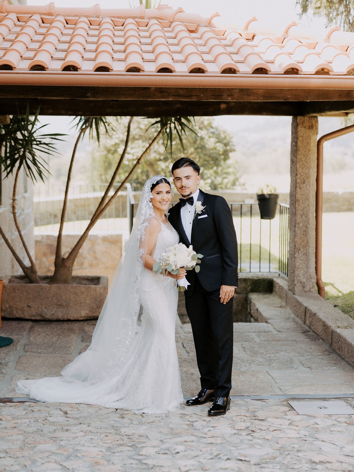A romantic wedding couple shares intimate moments under a covered walkway with Spanish-style terracotta roof tiles.