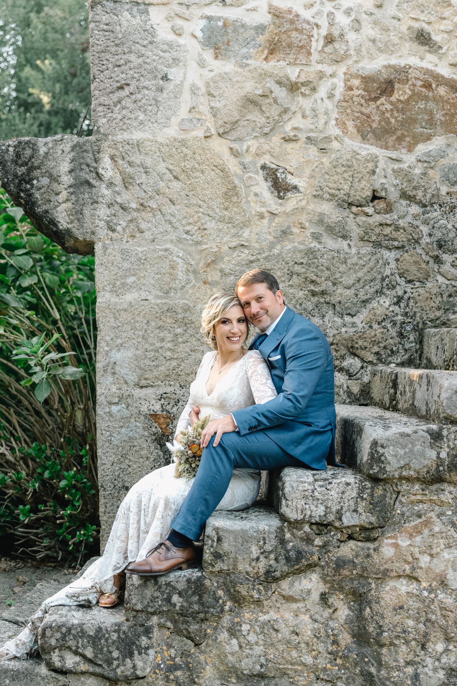 noivos senta-se junto em degraus de pedra encostados a uma parede rústica durante a sua casamento intimista em ponte de lima