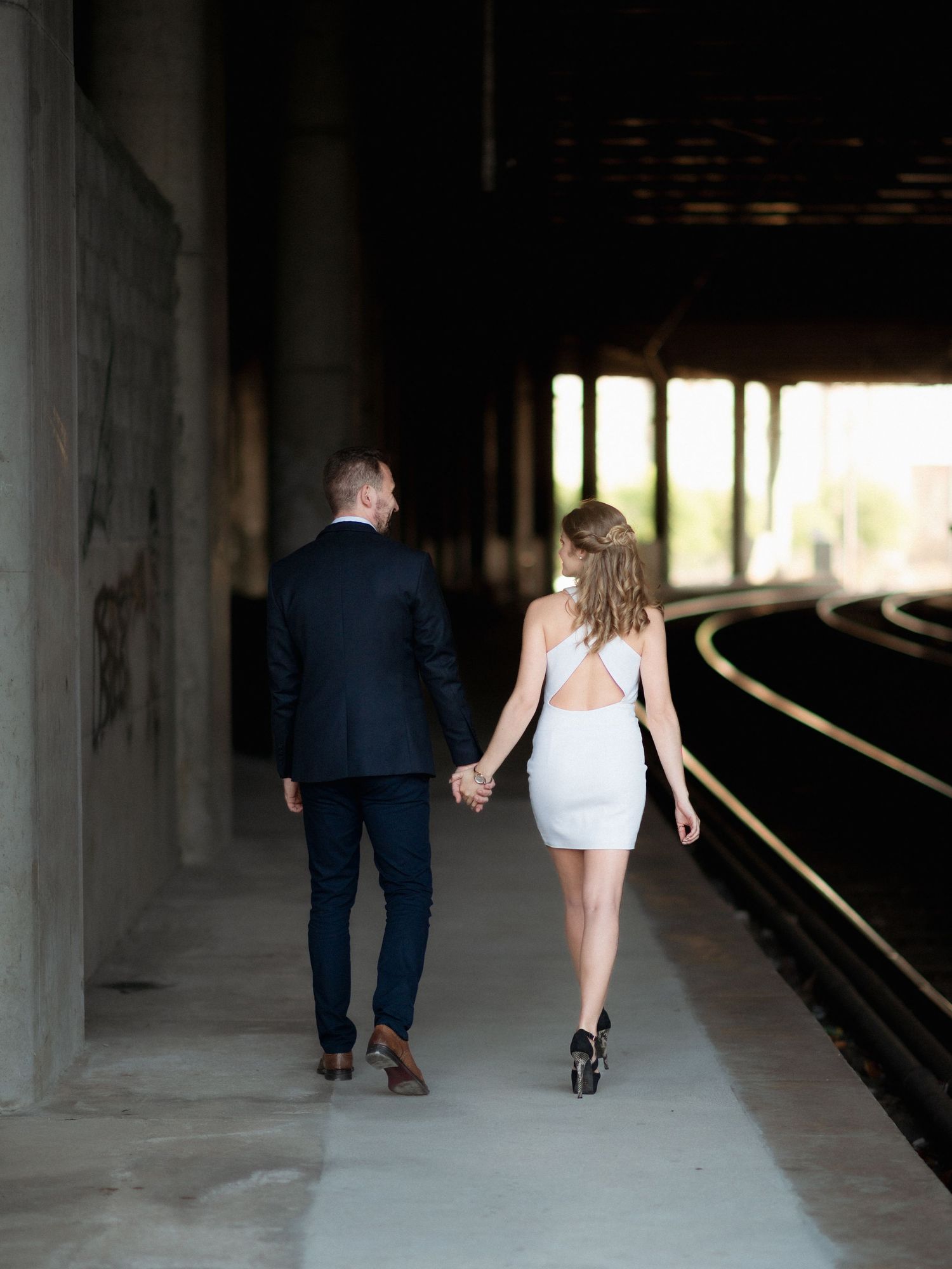 Um casal caminha de mãos dadas ao longo de uma plataforma de trem ao pôr do sol. Sessão fotográfica de namoro