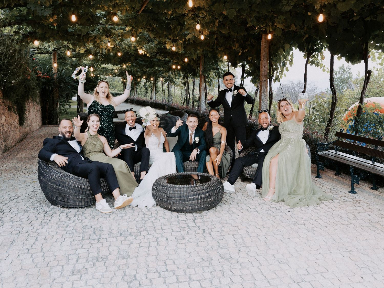Wedding party enjoys playful moments on outdoor tire swings at a rustic venue with string lights overhead.