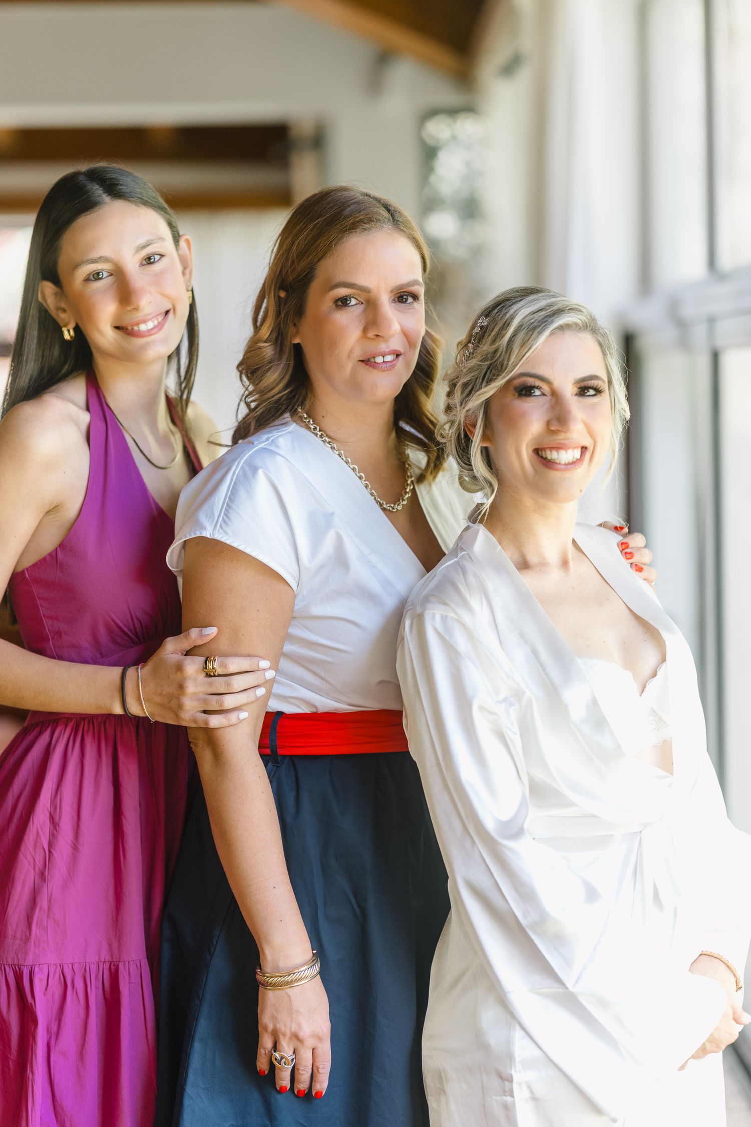A group of women in white and magenta dresses pose together in a bright indoor setting.