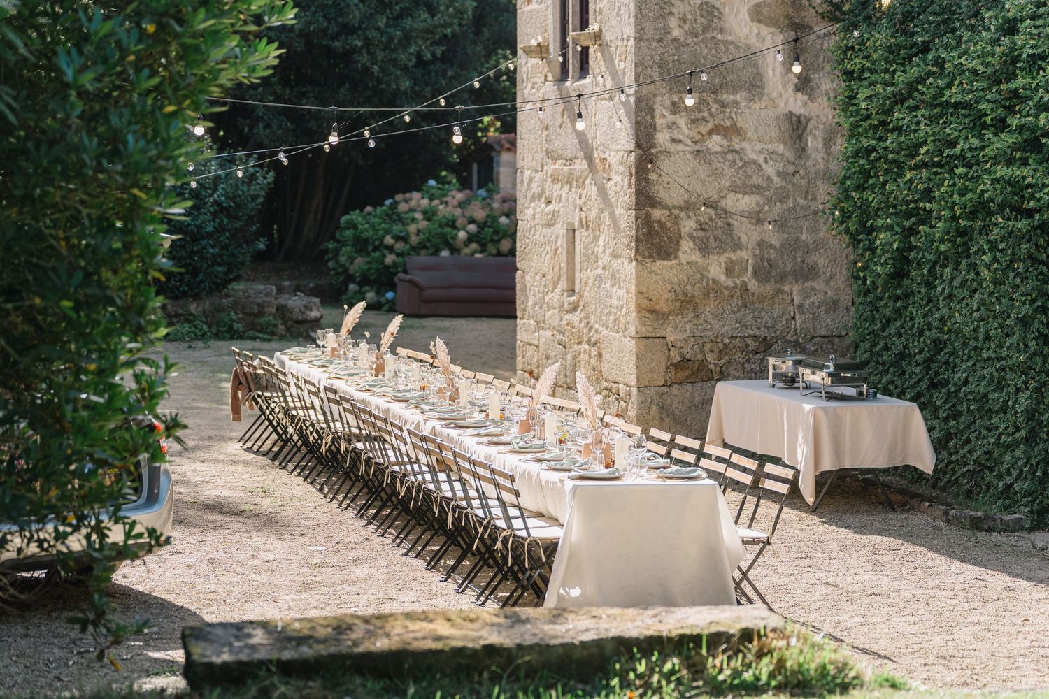 White folding chairs arranged in rows for an outdoor wedding ceremony at a rustic stone venue with string lights.