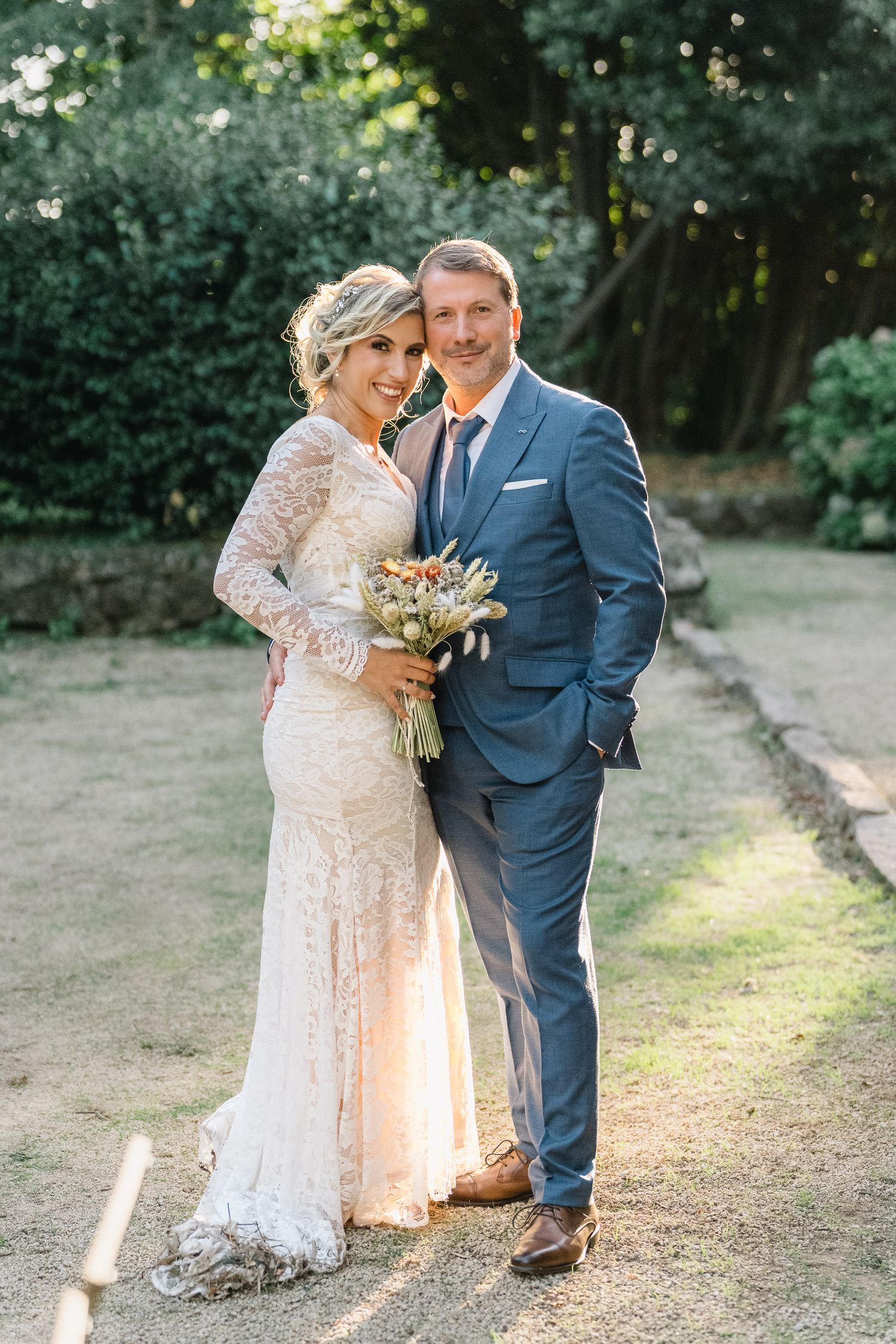 Noivos pousam ao ar livre, noiva com um vestido de renda a segurar um bouquet e o noivo com um fato cinzento. casamento em ponte de lima