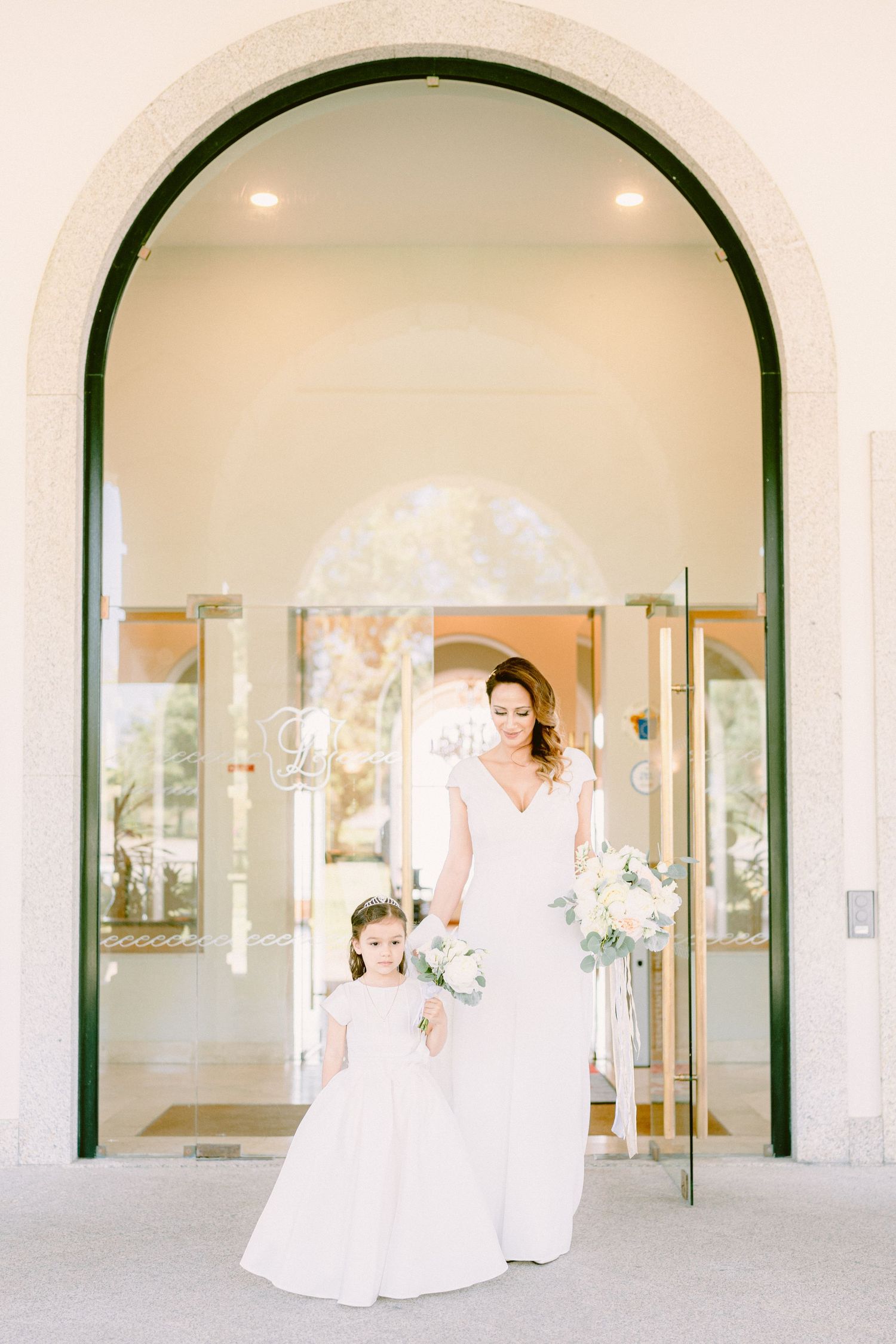 A series of elegant white archways frame a bridal scene in a light-filled gallery space.