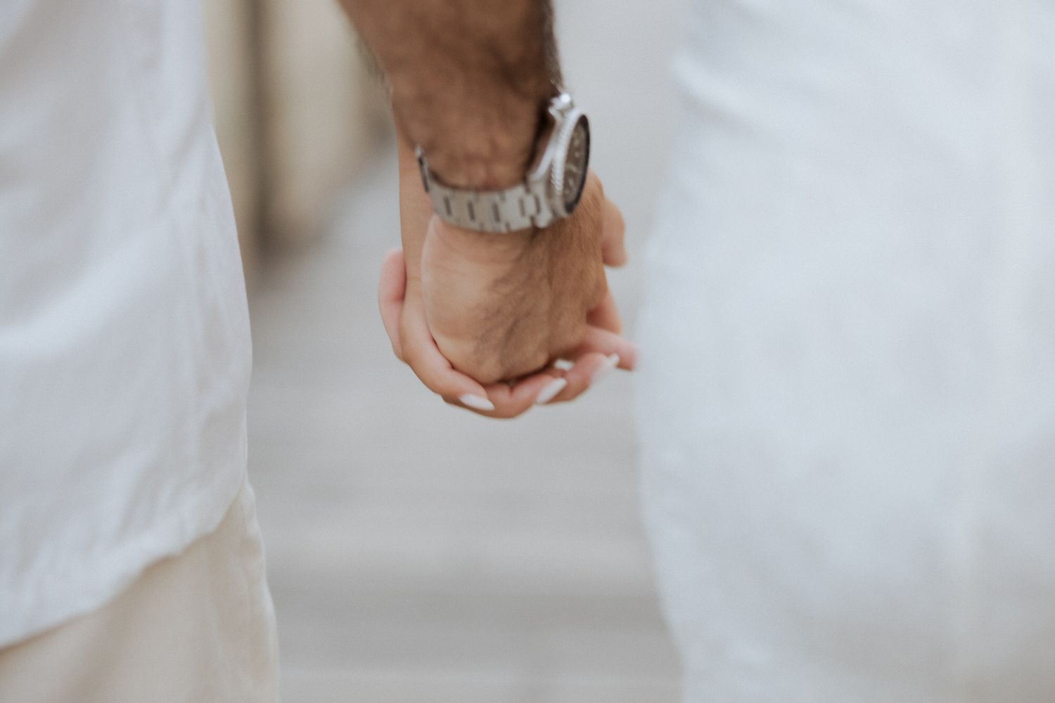 A bride and groom hold hands while walking through a light and airy venue space with white curtains.