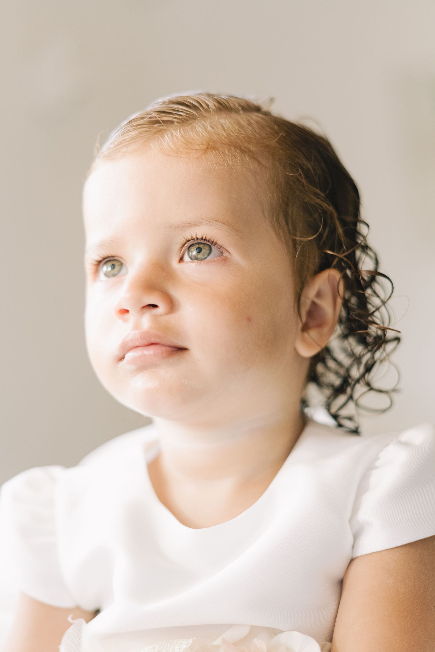 A series of close-up portraits showing a young child with curly hair and bright eyes looking upward in a white setting.