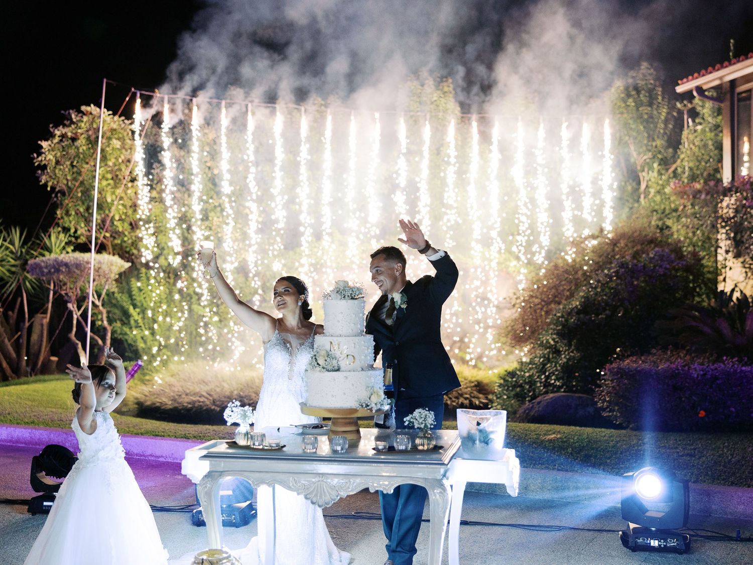 A series of wedding photos showing a couple dancing and posing by an illuminated fountain at an outdoor evening reception.