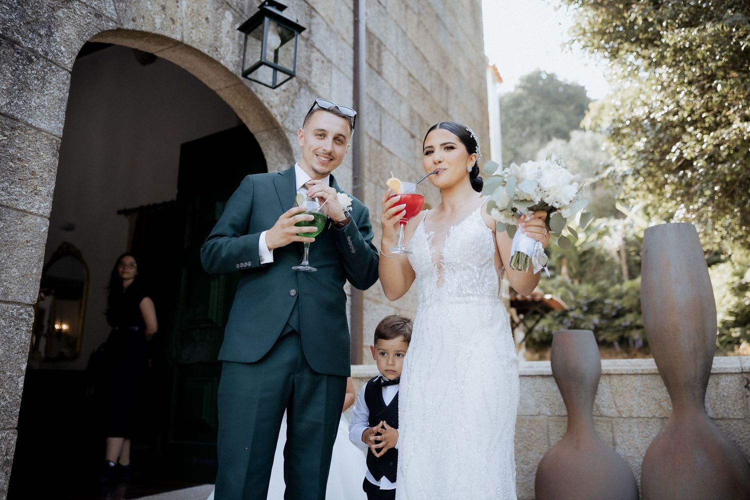 Wedding party gathered outside historic stone church during daytime celebration.