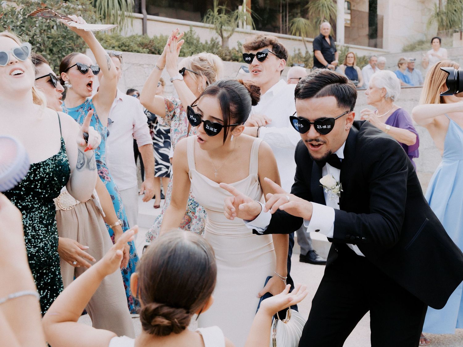 Wedding guests dance and celebrate on an outdoor patio during a daytime reception party.