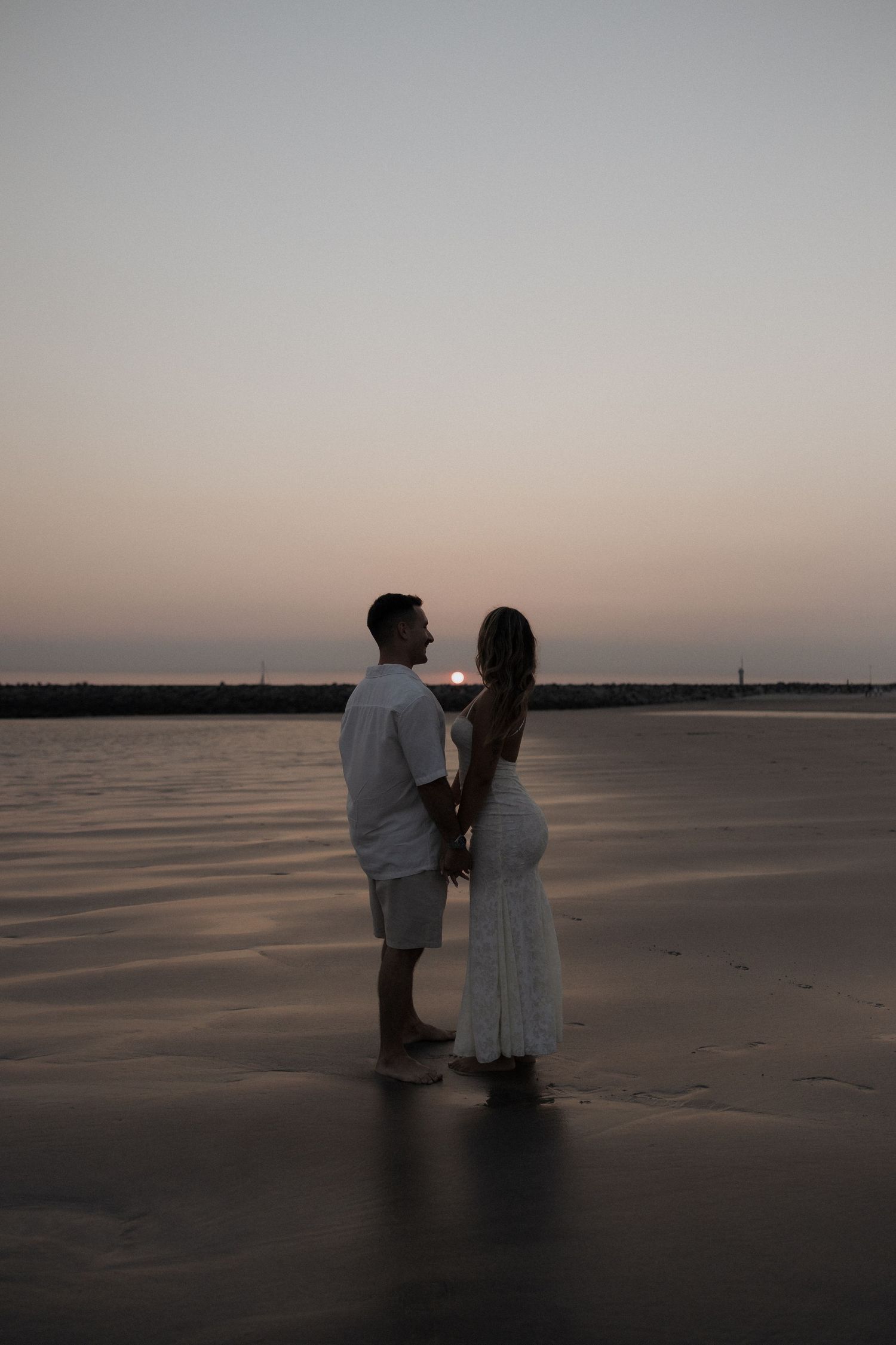 Silhueta de um casal em pé na praia ao pôr do sol. Sessão fotográfica na praia em Viana do Castelo