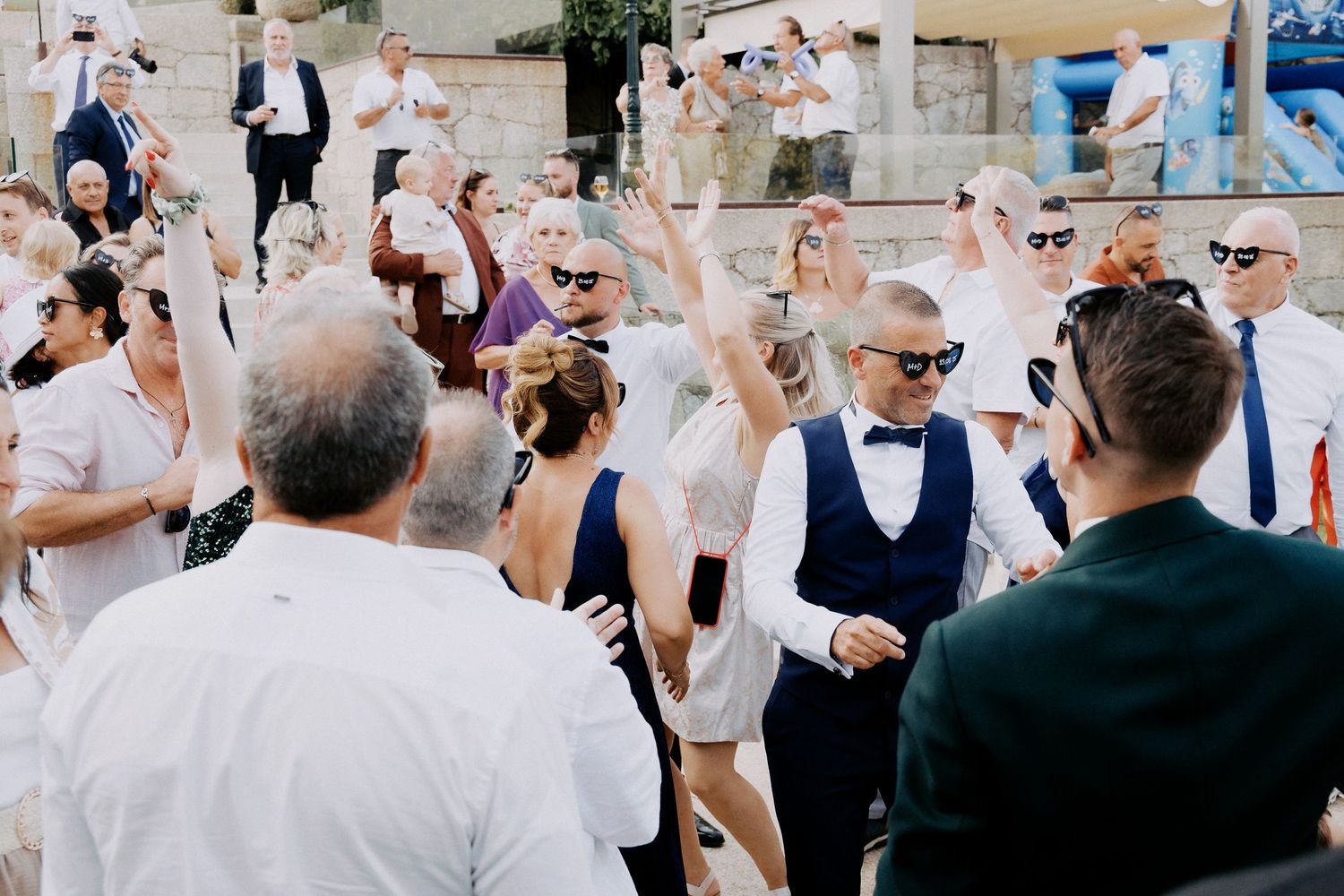 Wedding guests celebrate and dance together at an outdoor reception while tossing white confetti in the air.