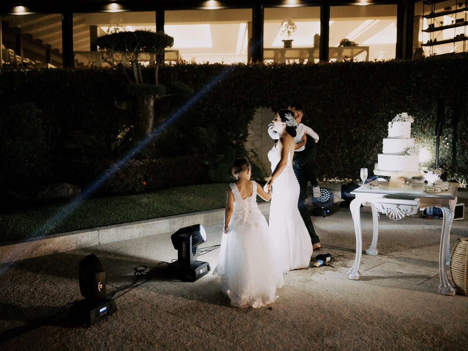 An elegant outdoor evening wedding reception with a white tiered cake displayed on an ornate table.
