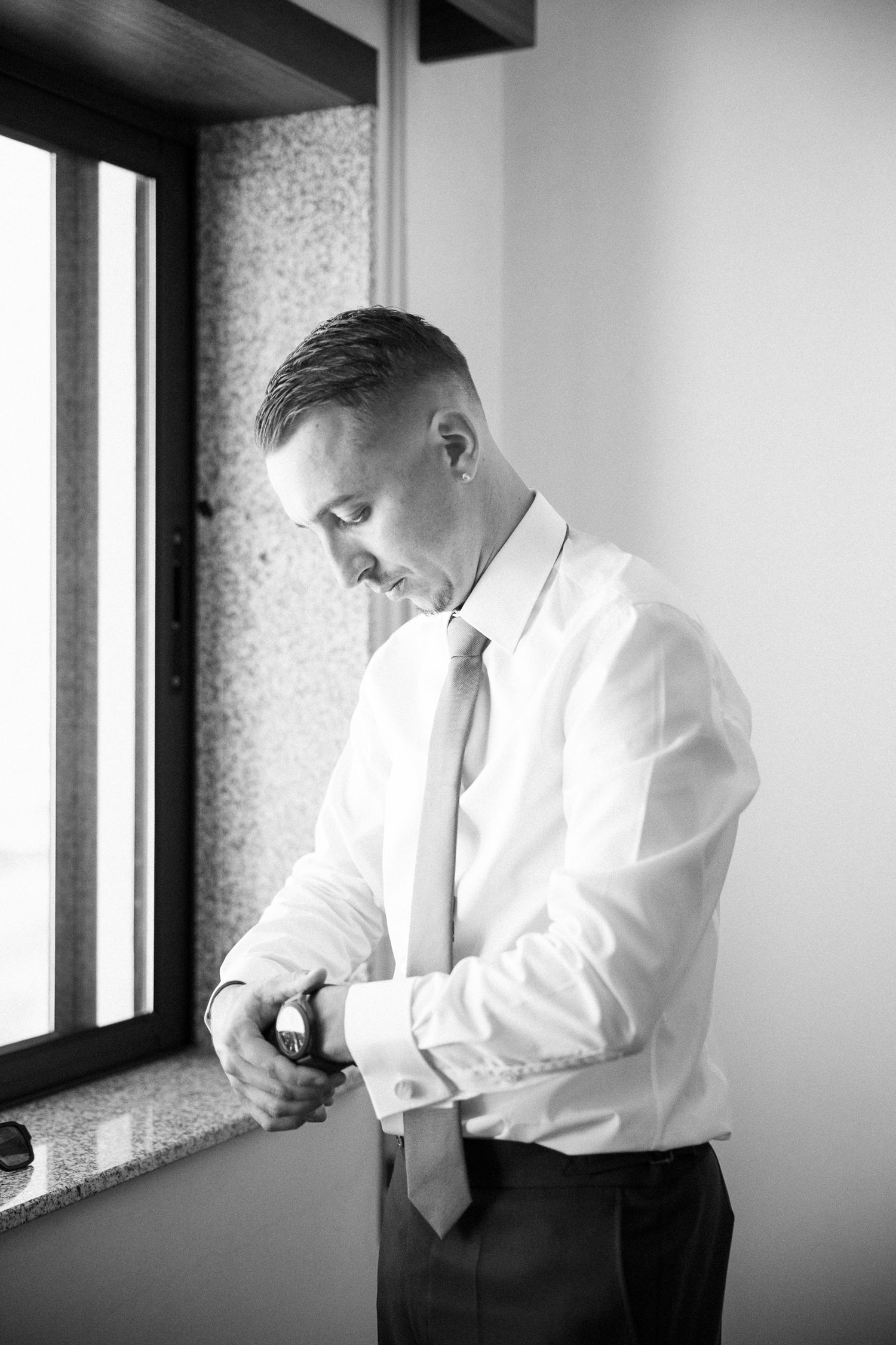 Black and white photo series of someone adjusting their tie near a window, creating a dramatic lighting effect.