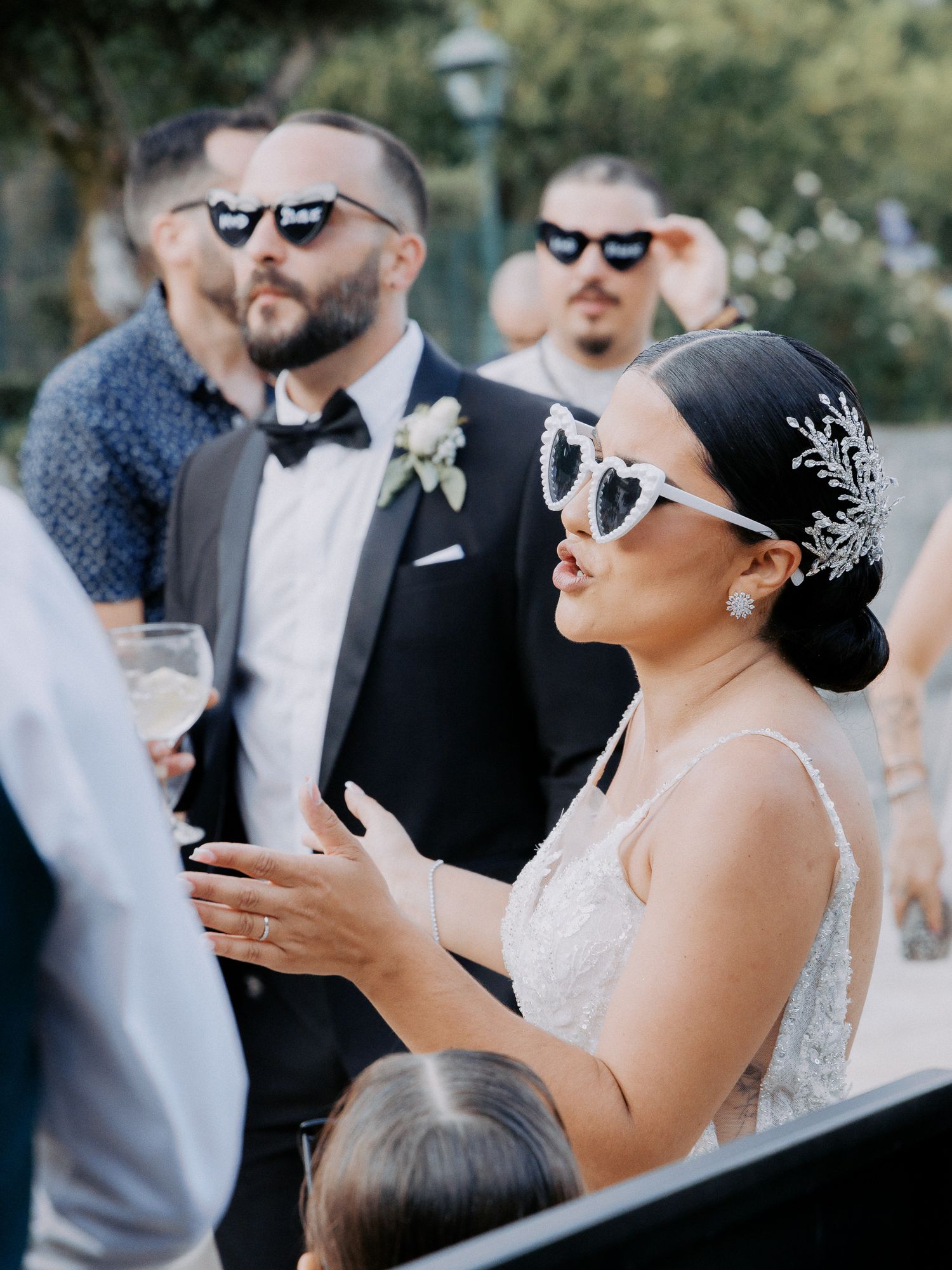 Wedding guests wearing stylish sunglasses share a fun moment during an outdoor celebration.