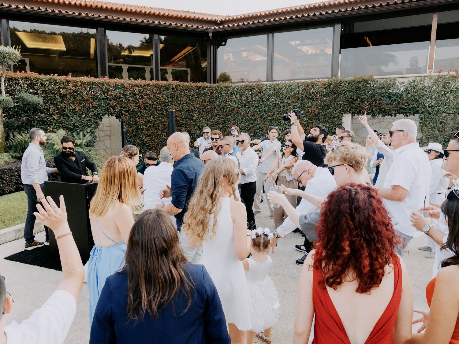 Wedding guests gather outdoors in a garden setting for a celebration with white decor and floral arrangements.