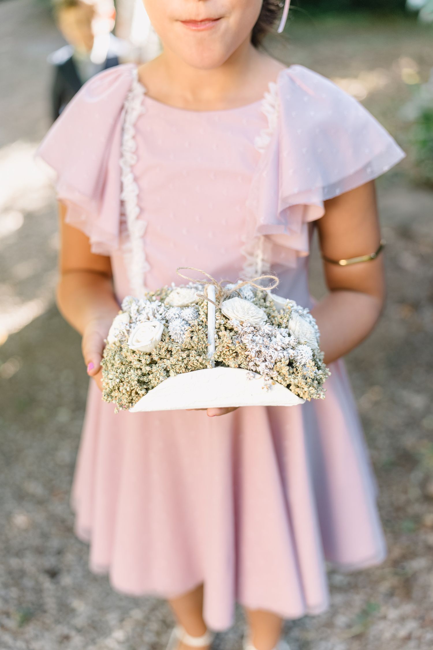 A person wearing a soft pink flutter sleeve dress with a delicate floral crown made of baby's breath flowers.