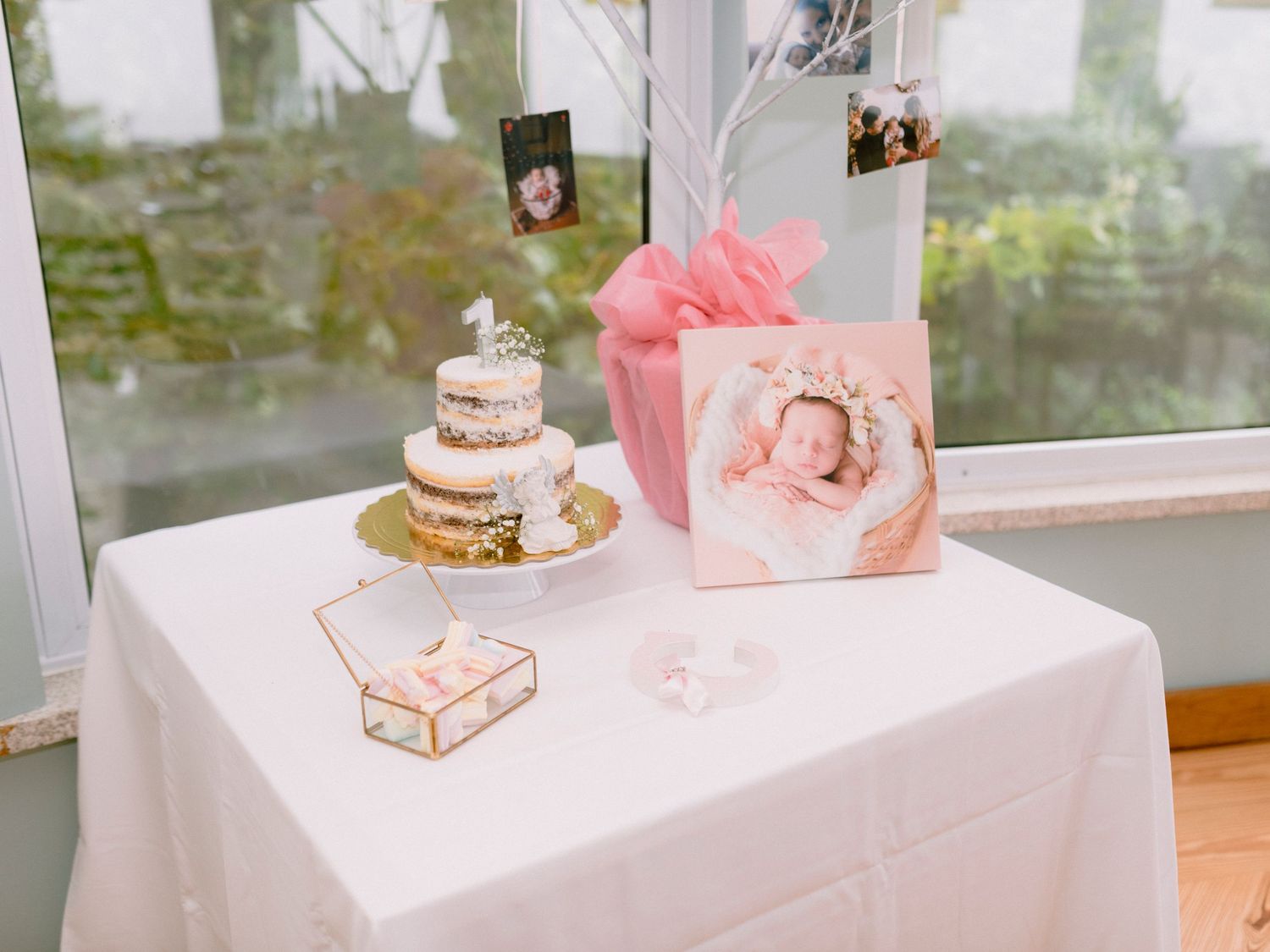 A white dessert table decorated with pink accents and floral arrangements displays elegant treats and cakes.
