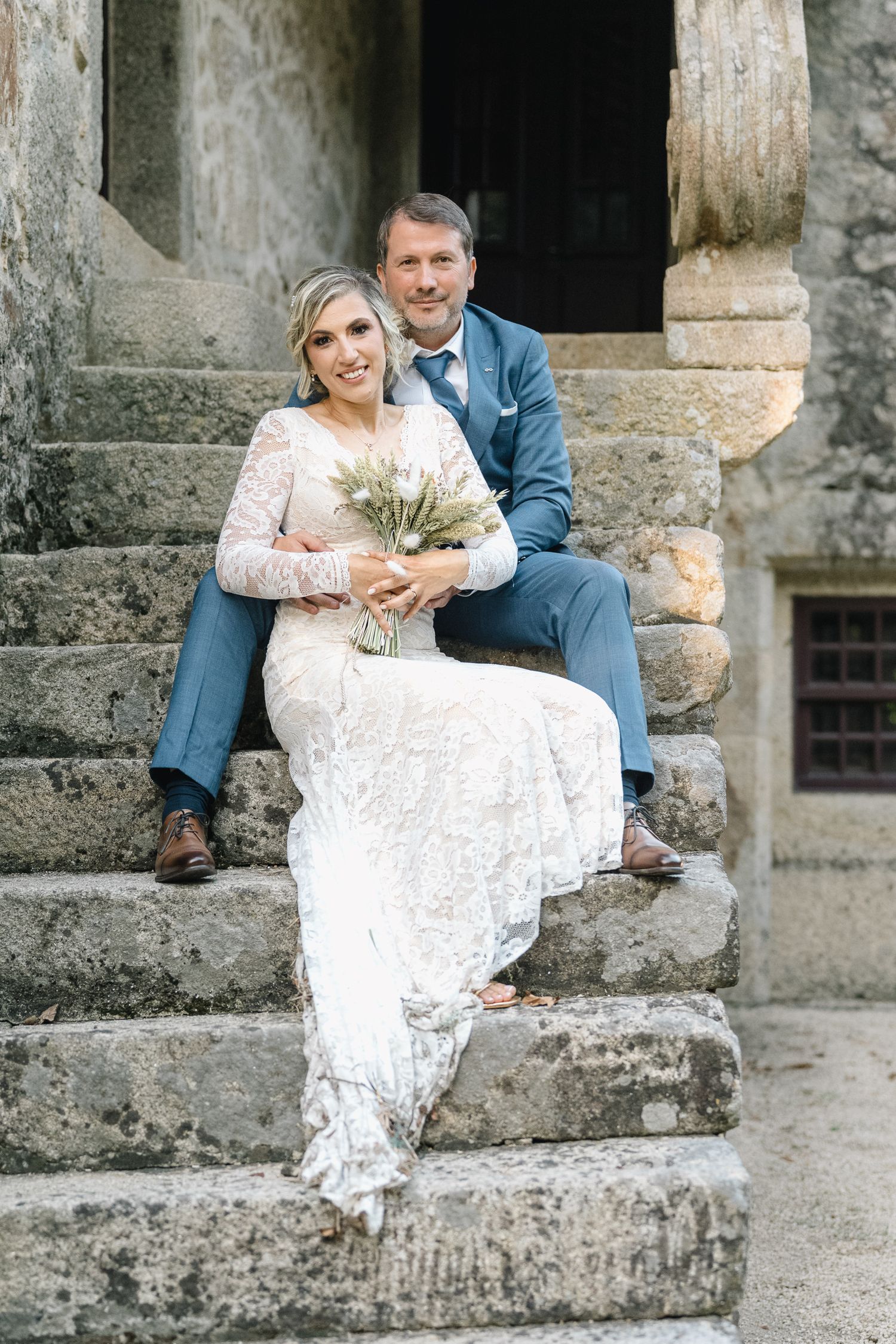 Um casal com trajes de casamento senta-se junto em degraus de pedra num local rústico. Casamento rustico em ponte de lima