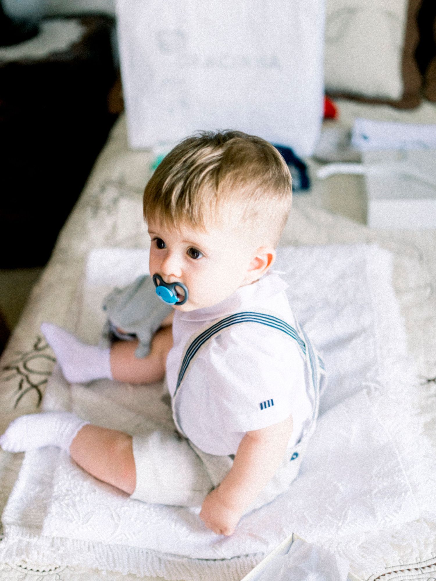 Baby in white clothing crawls and explores on a textured white surface in a series of candid moments.
