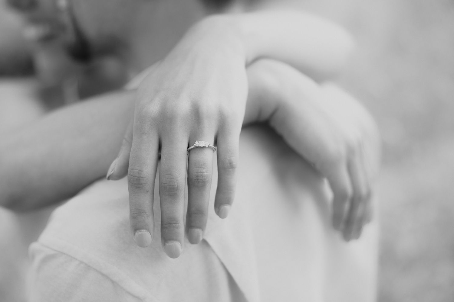 Detalhe em preto e branco, em close-up, de mãos com anel de noivado.