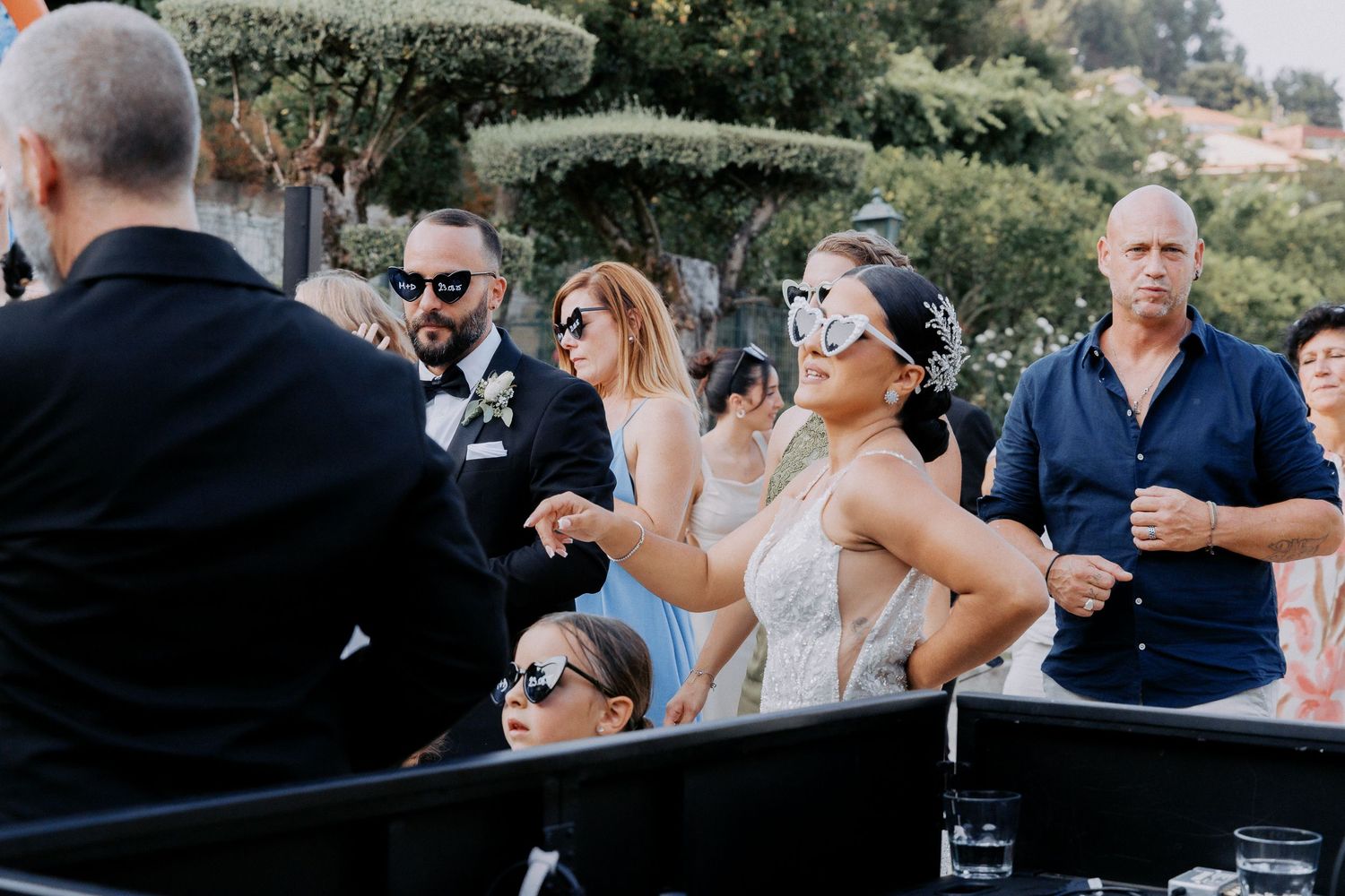 Wedding guests in sunglasses enjoy drinks and conversation during an outdoor reception celebration.