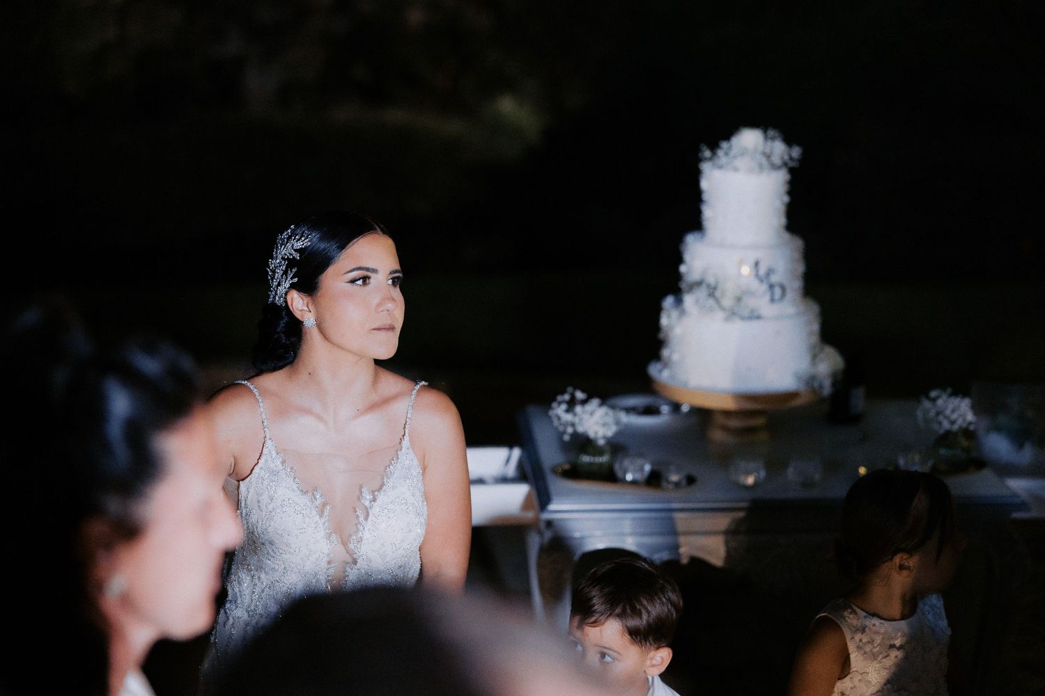 A white wedding cake sits on a display table during an evening reception.