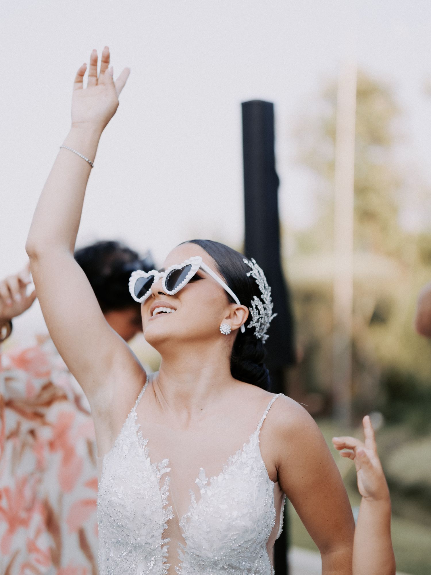 A joyful celebration moment with raised arms and white lace dress against a sunlit outdoor backdrop.