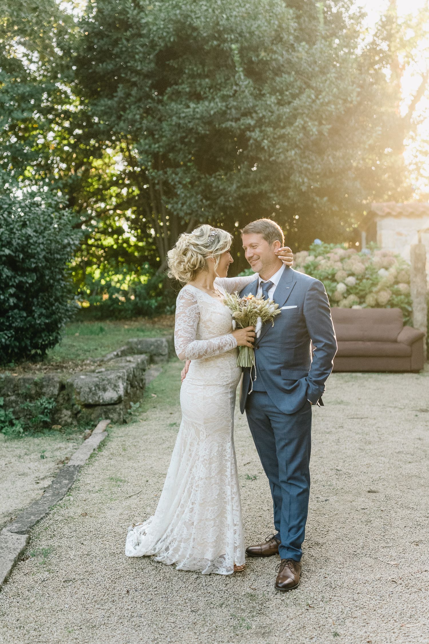 Um casal partilha um momento romântico num jardim durante o seu casamento, com a bela luz do sol a filtrar-se através das árvores.