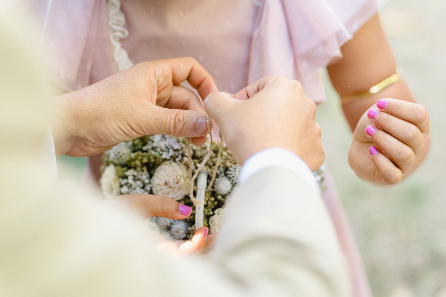 Grande plano de mãos a segurar delicadas flores de gypsophila e pétalas de rosa cor-de-rosa sobre um fundo suavemente desfocado.